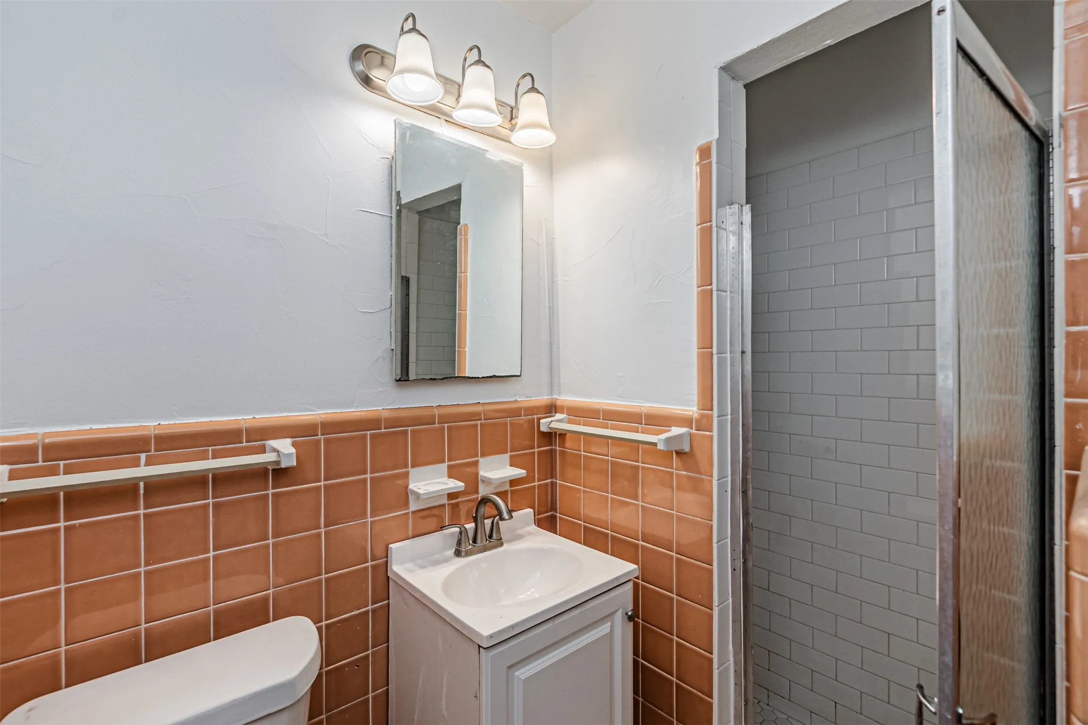 Shower enclosure with a sliding door, white subway tile shower surround, and a vanity with a white ceramic sink