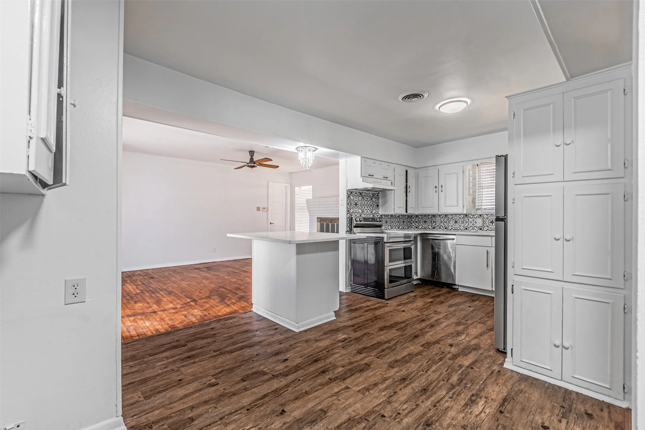 Kitchen featuring wood-finish flooring, white cabinetry, a kitchen island with a white countertop, stainless steel appliances, and a patterned tile backsplash