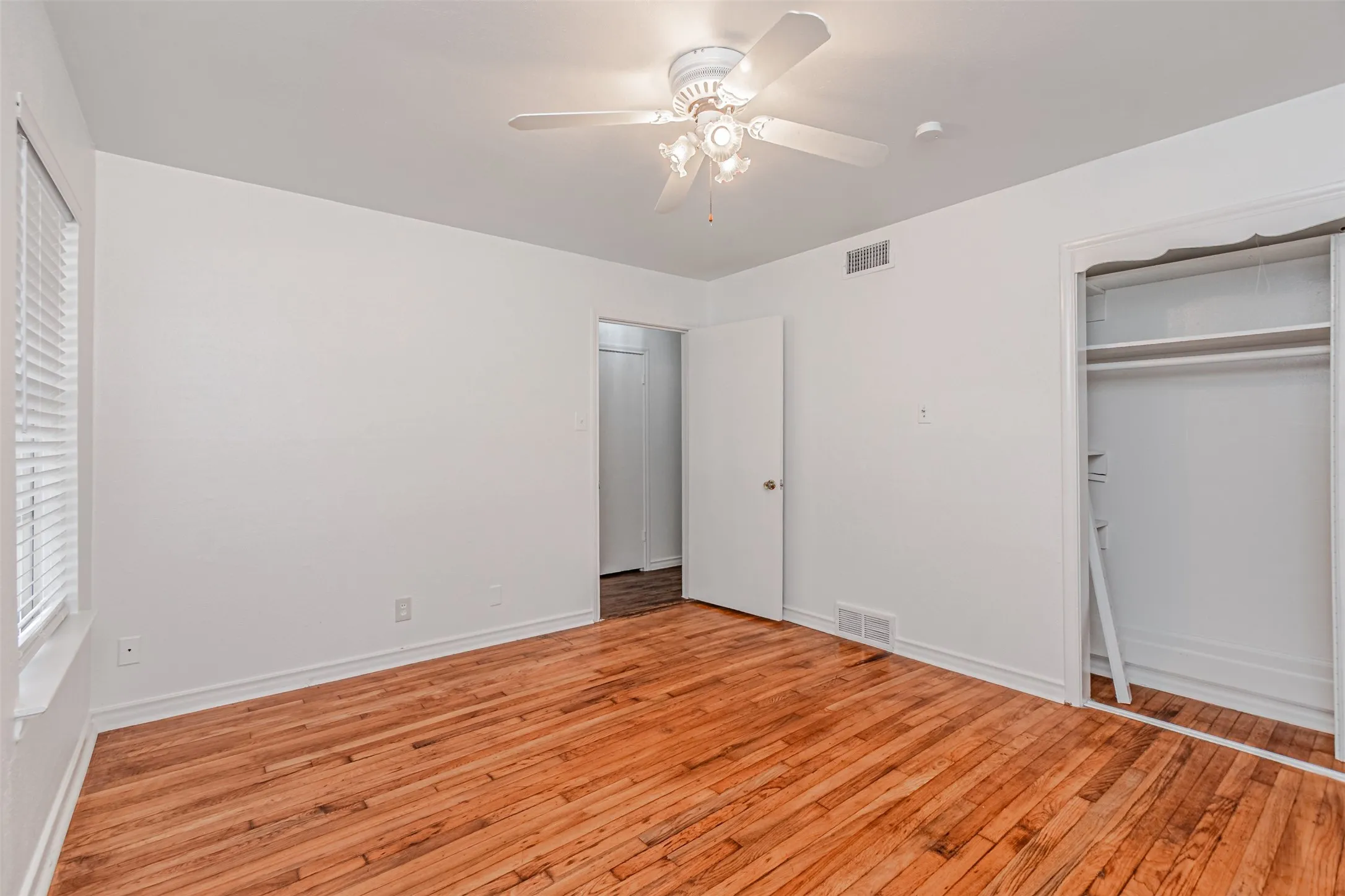 Hardwood flooring throughout, white walls, ceiling fan with integrated lighting, and a closet with sliding doors