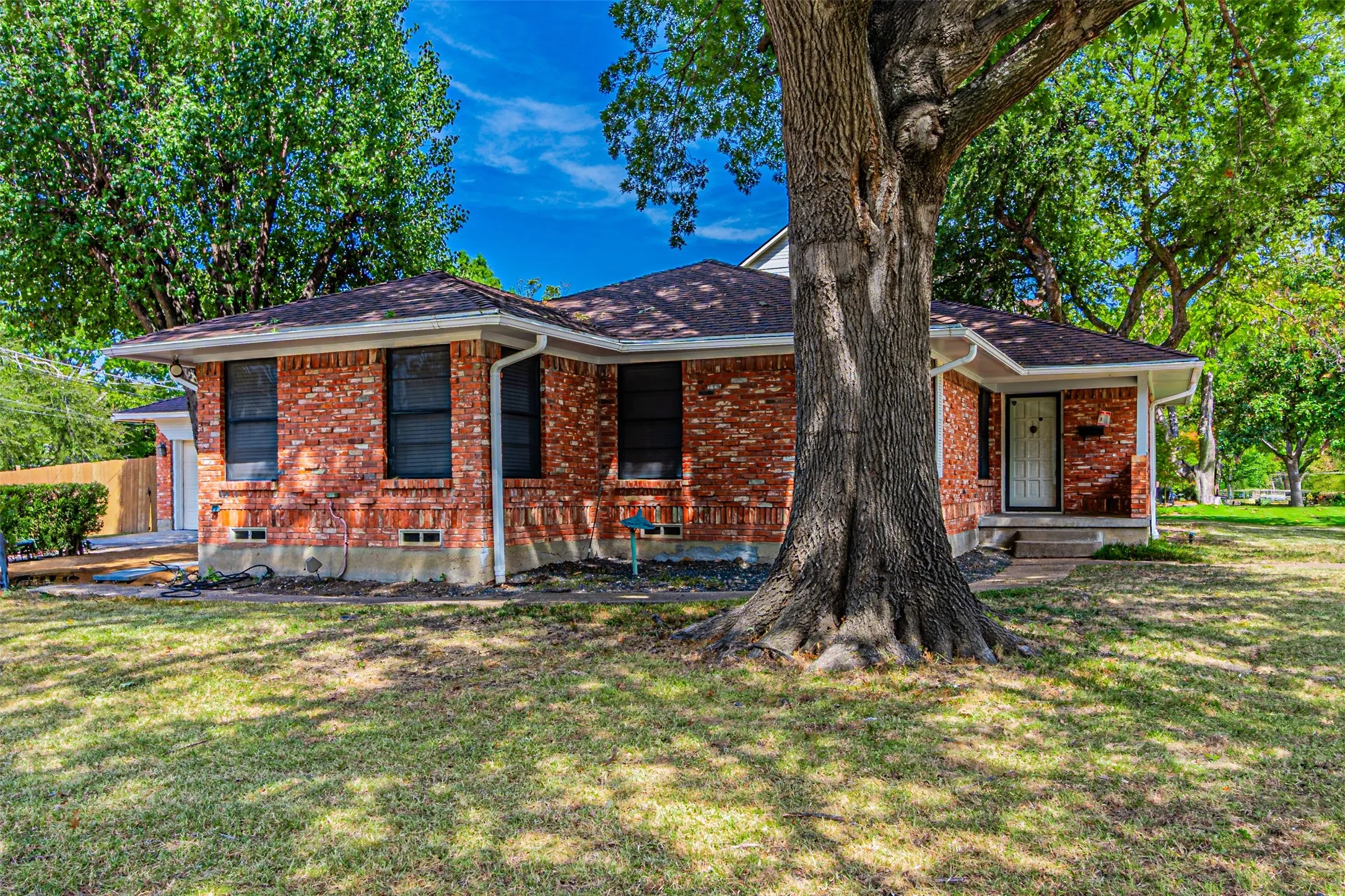 Brick exterior, dark shingle roof, white trim, covered front entry, and a mature tree