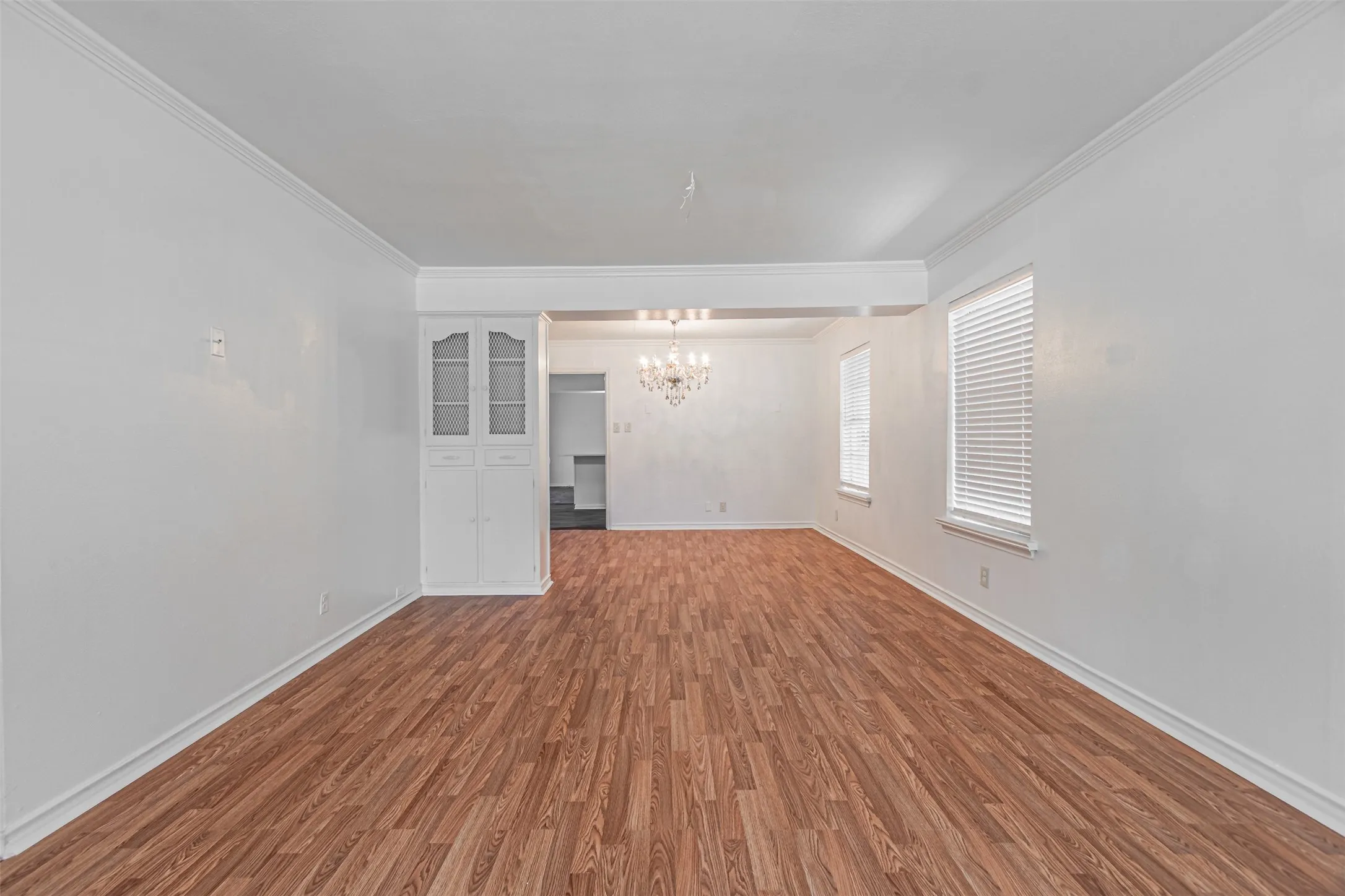 Wood-finish flooring, crown molding, built-in cabinetry, and white window blinds