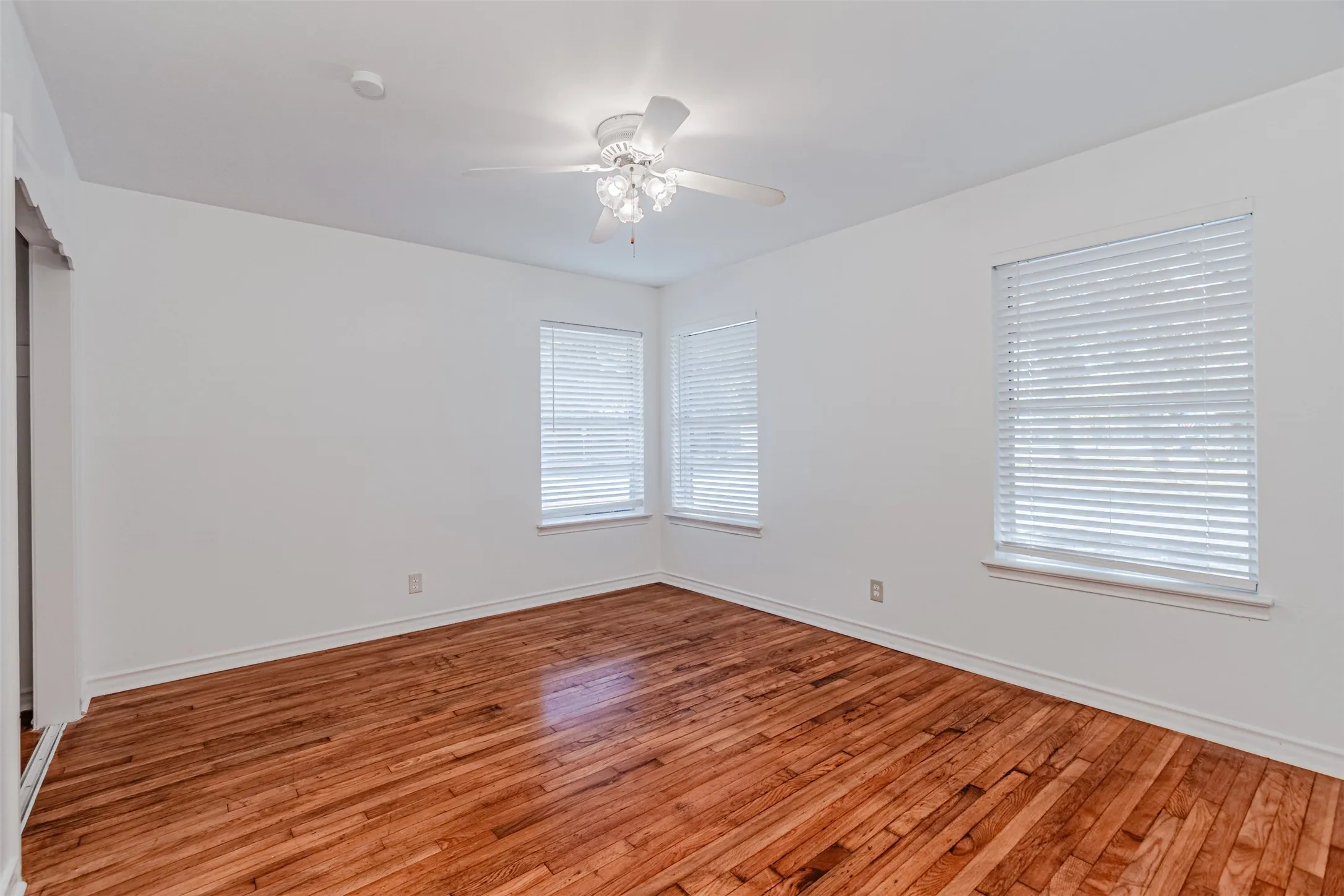 Hardwood flooring throughout, multiple windows with blinds, ceiling fan with integrated lighting, white walls, and white trim
