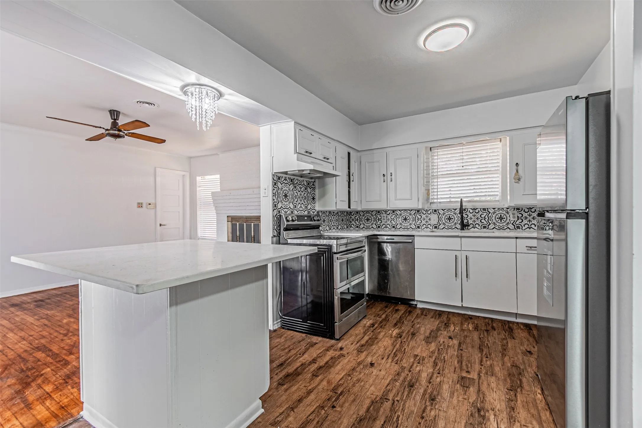 Kitchen featuring stainless steel appliances, patterned tile backsplash, white cabinetry, and wood-finish flooring