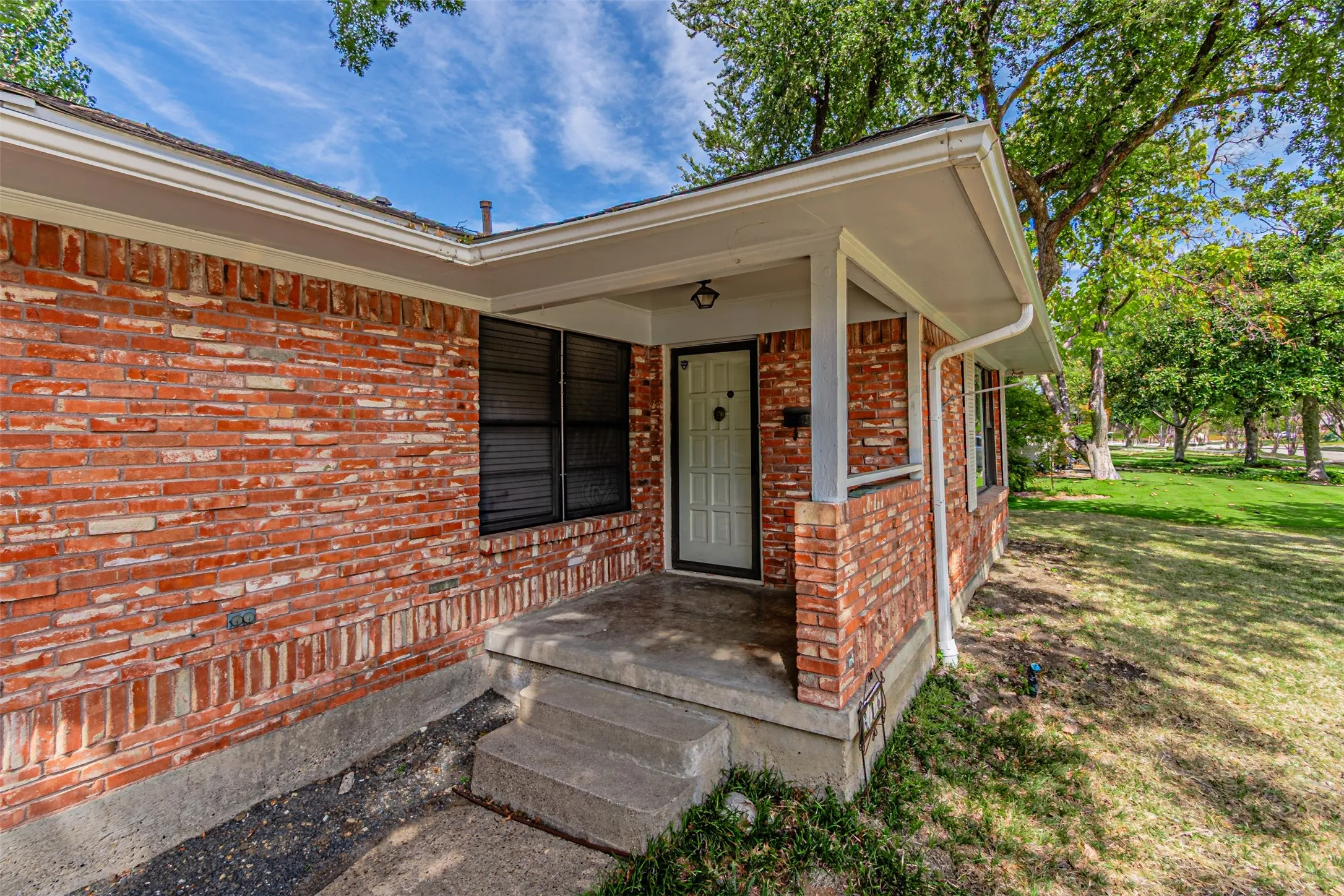 Brick exterior with covered front porch, concrete steps, and white trim