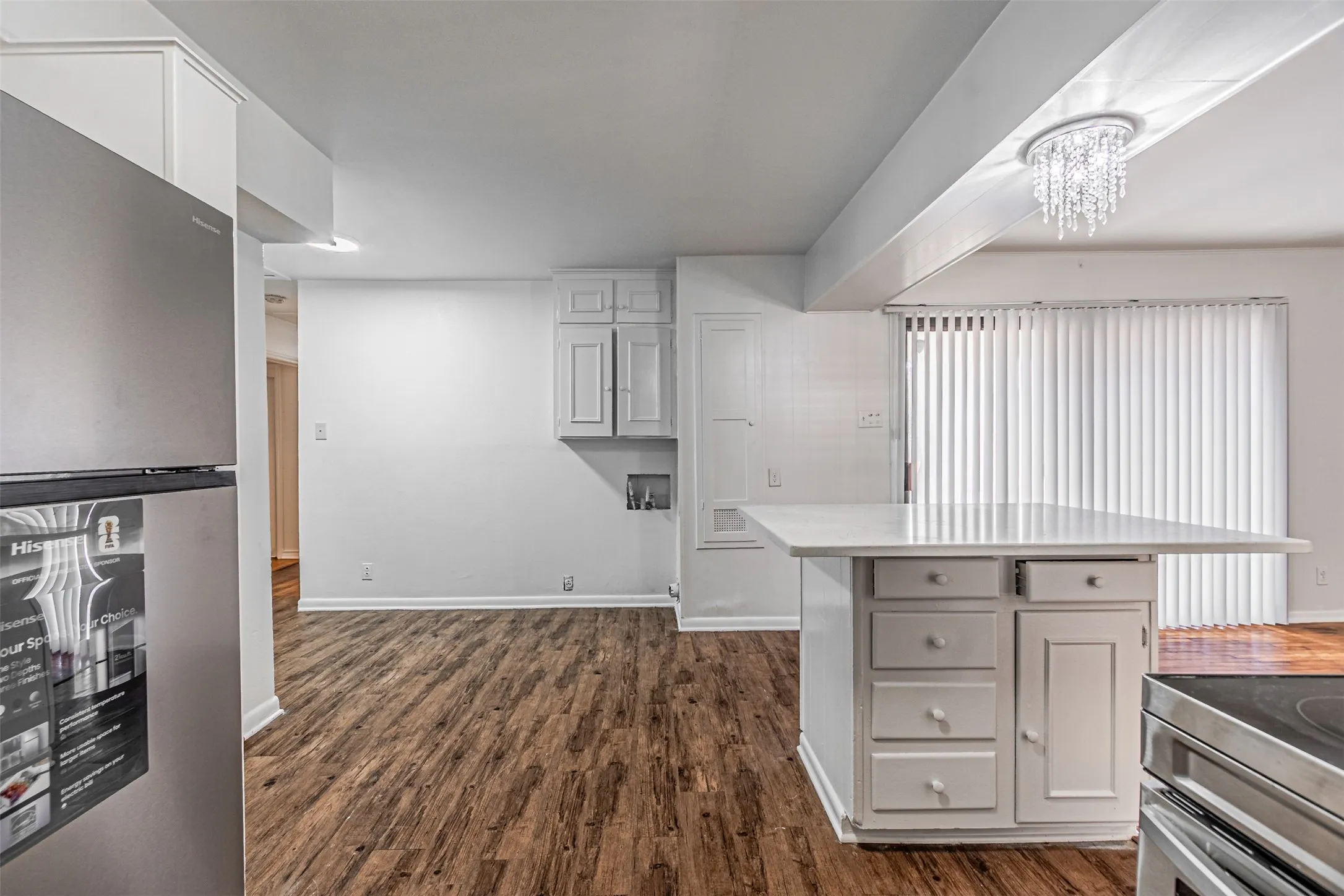 Wood-finish flooring, white cabinetry, island with countertop, and a chandelier-style light fixture