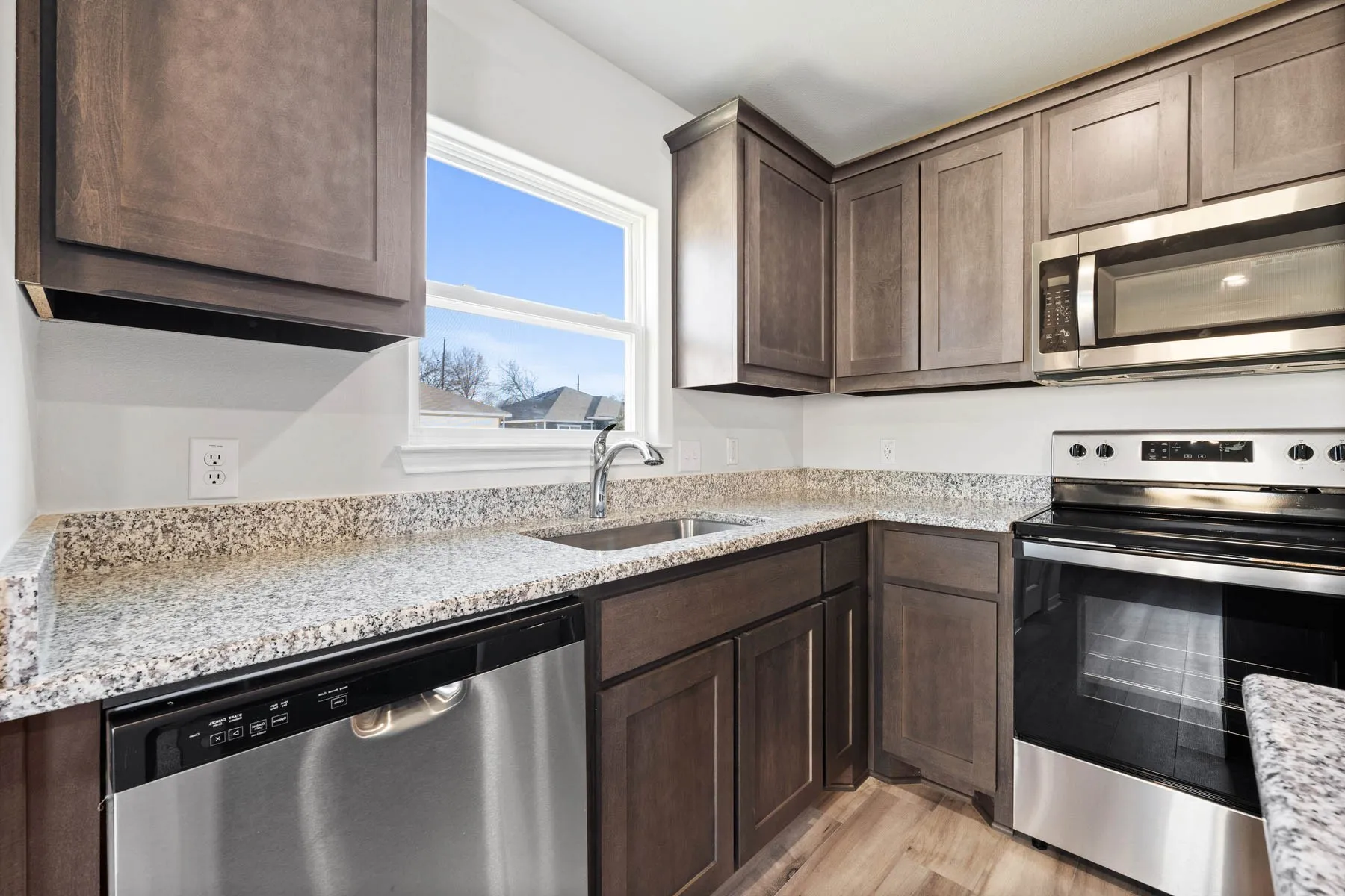 Kitchen with dark brown cabinetry, light stone countertops, sink, light hardwood / wood-style floors, and appliances with stainless steel finishes