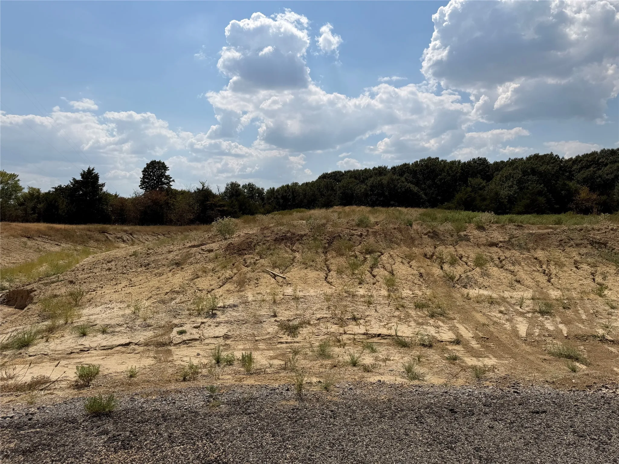 Raw land featuring a gravel foreground, varied topography, and a distant tree line