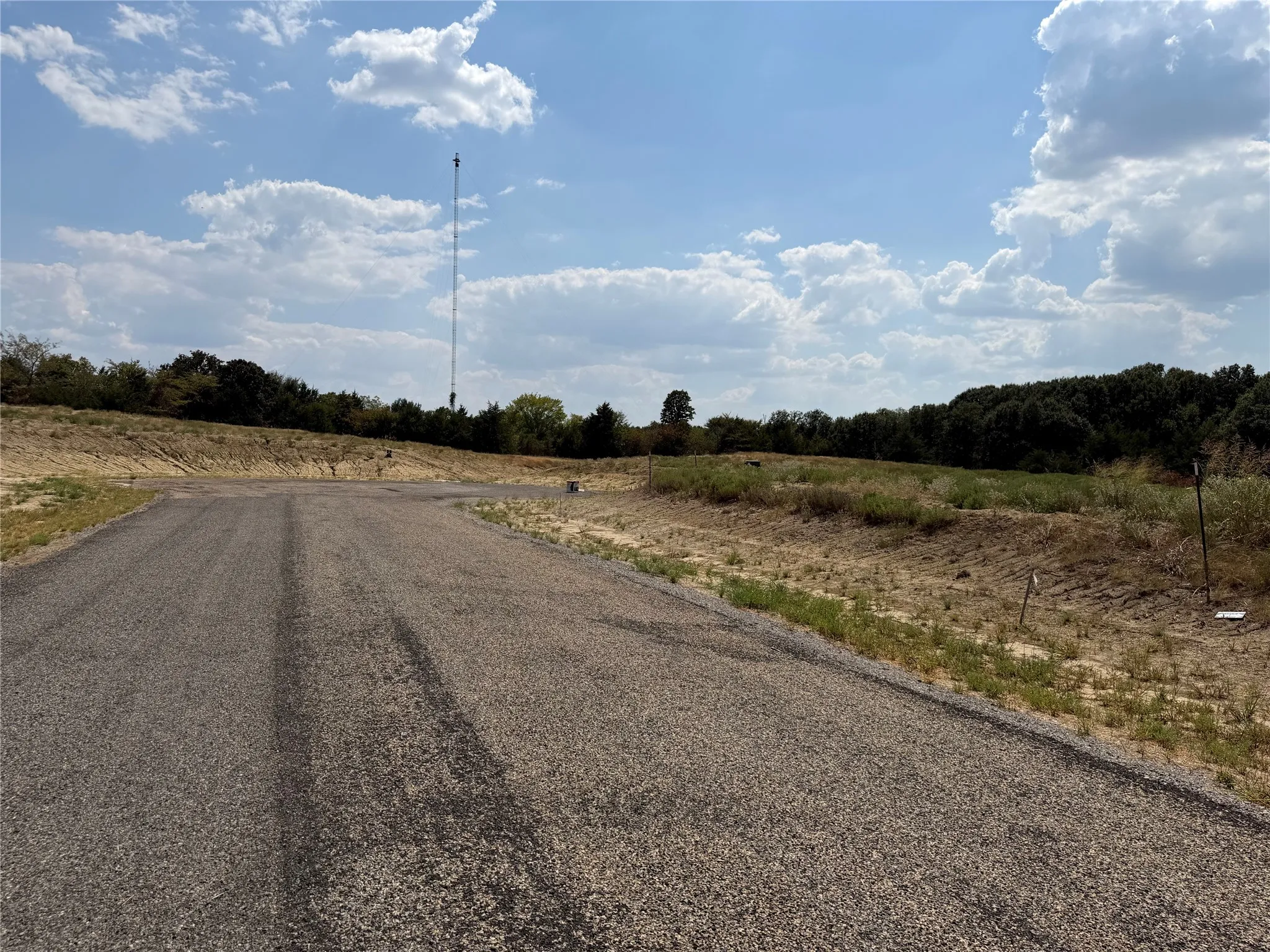 Paved road access leading to undeveloped land with a distant tree line