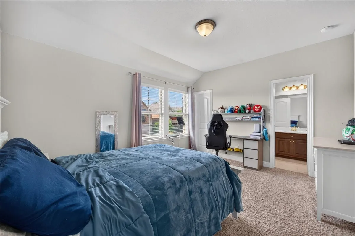 Neutral wall paint, carpet flooring, arched ceiling, and an en-suite bathroom with a wood-finish vanity