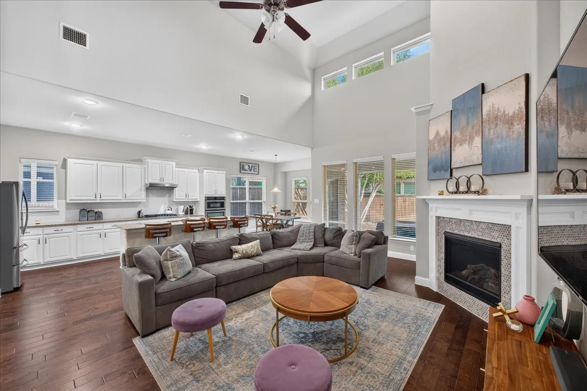 Vaulted ceiling with a ceiling fan, wood-finish flooring, white cabinetry, integrated oven, and a tiled fireplace