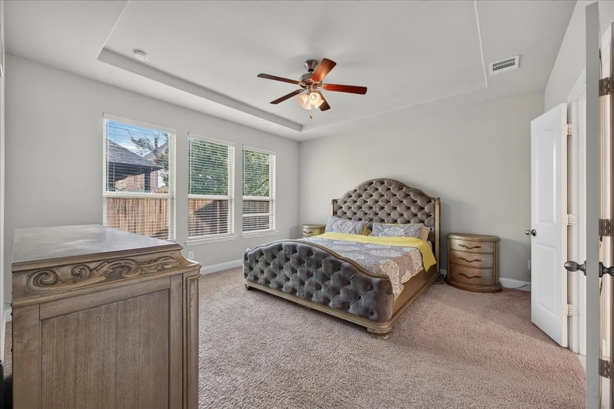 Recessed tray ceiling with a ceiling fan, three windows with blinds, and neutral wall paint