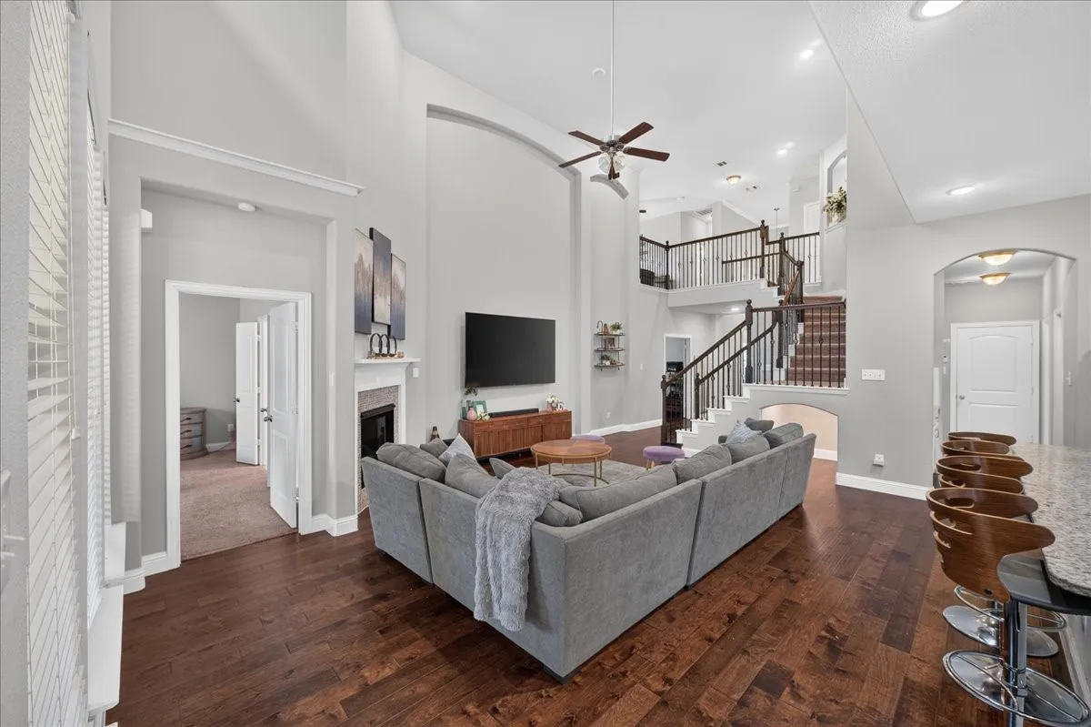 Hardwood-style flooring throughout the main living area, fireplace with mantel, two-story ceiling, and a multi-level staircase with dark wood railings