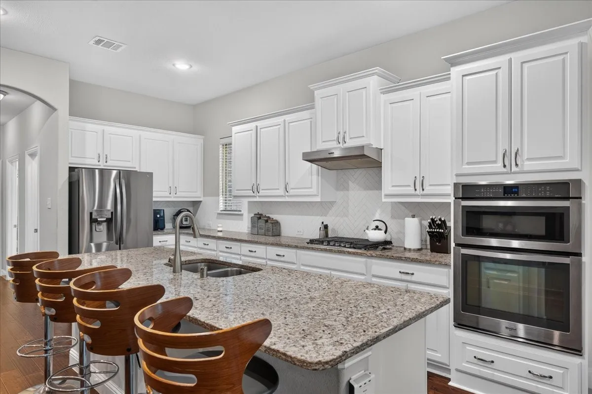 White shaker cabinetry with crown molding, granite countertops, stainless steel appliances, a built-in oven with microwave, and wood-finish flooring