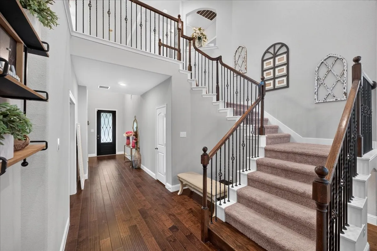 Hardwood-finish flooring, two-story foyer, carpeted staircase with wrought iron balusters, wood handrails, and a transom window above the entry