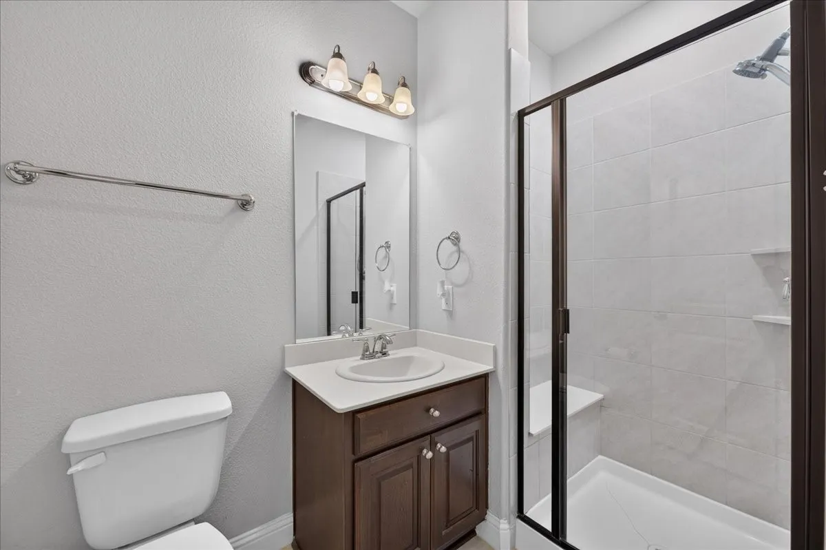 Bathroom featuring a dark wood-finish vanity, white countertop with an undermount sink, and a glass-enclosed shower with a built-in bench