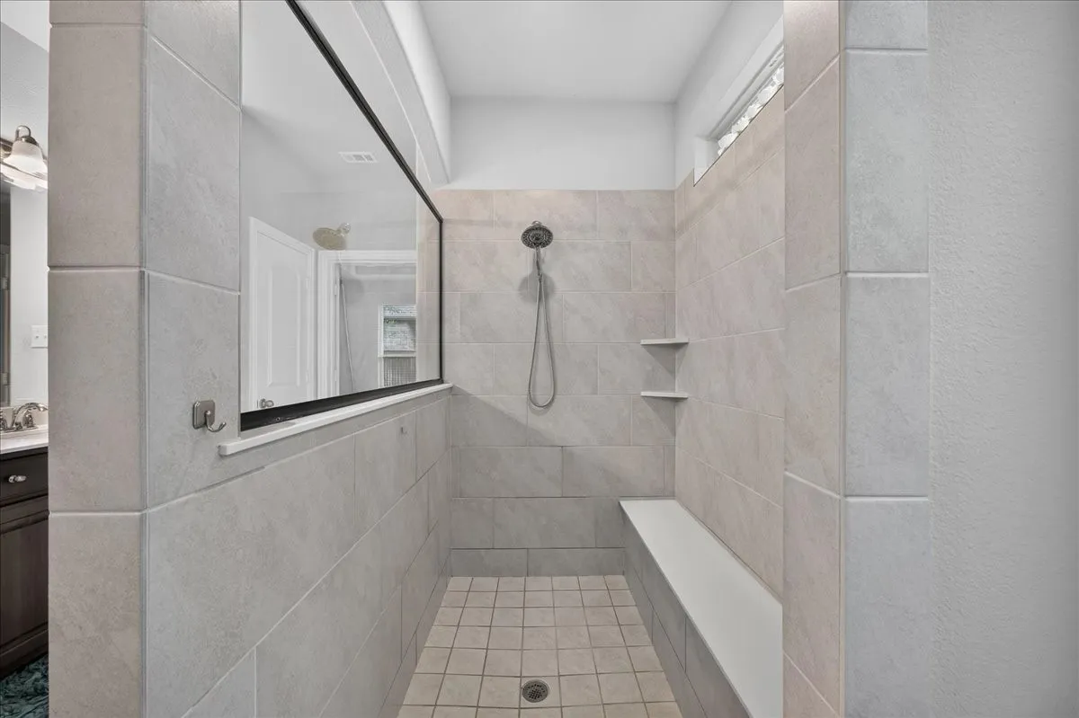 Expansive shower stall featuring light-toned tile, a built-in bench, two recessed shelves, and a large fixed glass panel