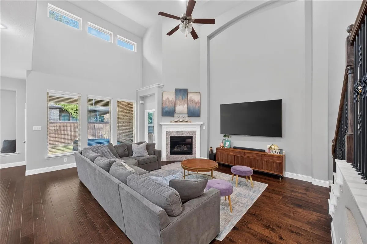 Spacious living area featuring high ceilings, wood-finish flooring, multiple windows, a ceiling fan, and a fireplace with a decorative mantel