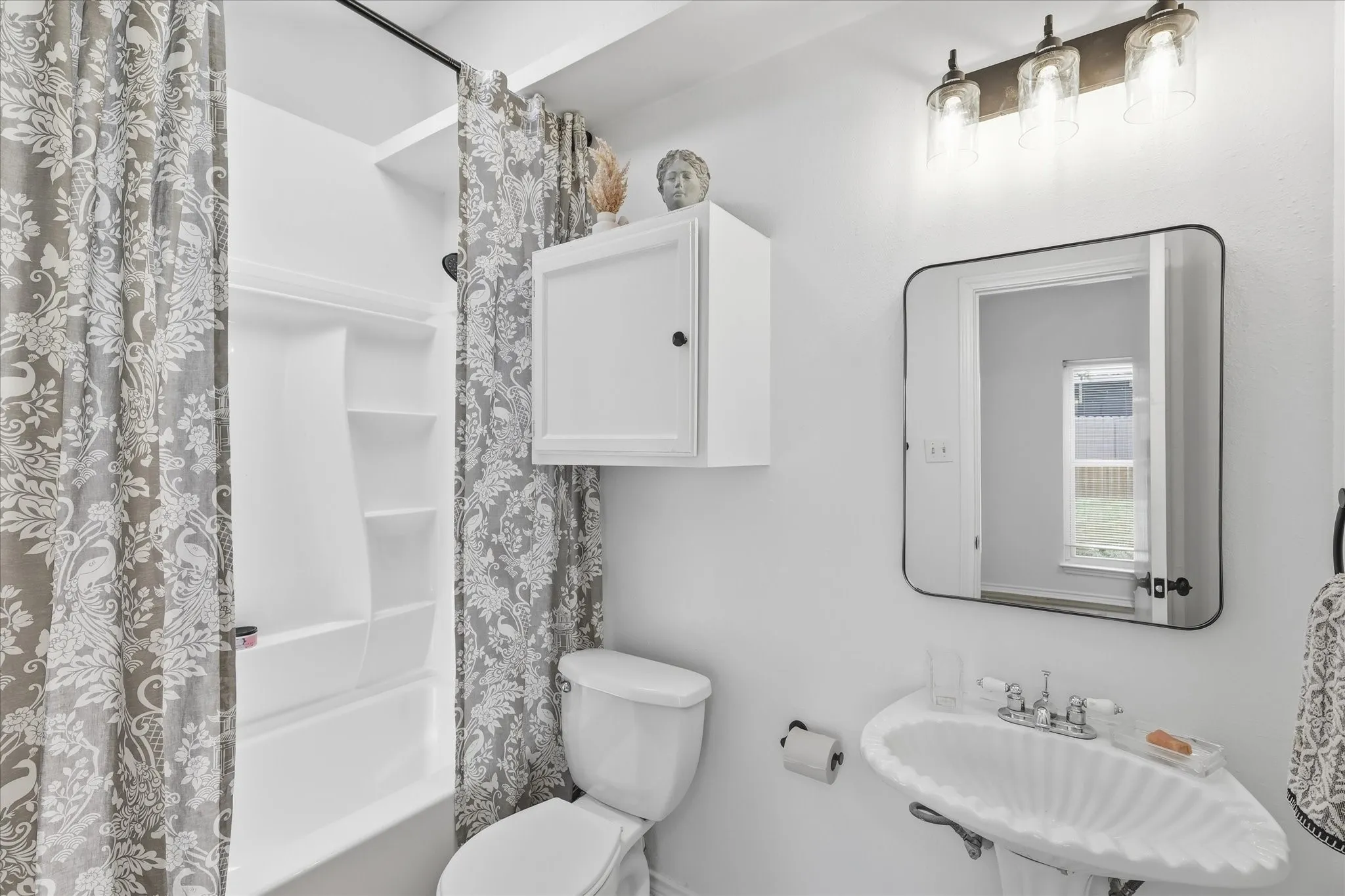 White pedestal sink with chrome faucet, wall-mounted light fixture, rectangular mirror, and a white medicine cabinet