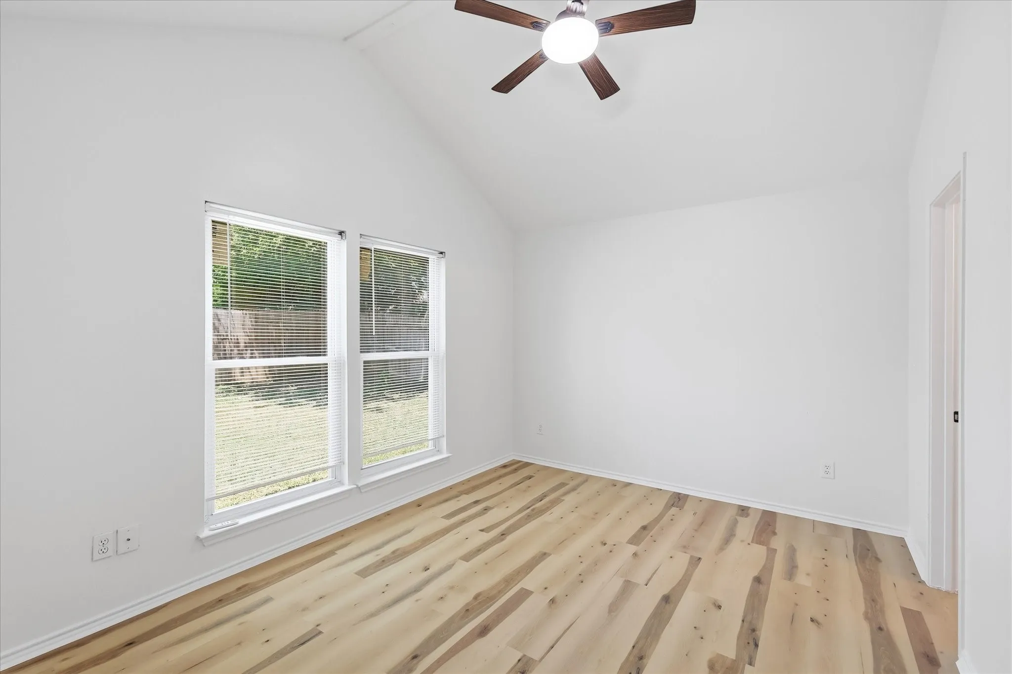 Vaulted ceiling with a ceiling fan, dual windows, and wood-finish flooring