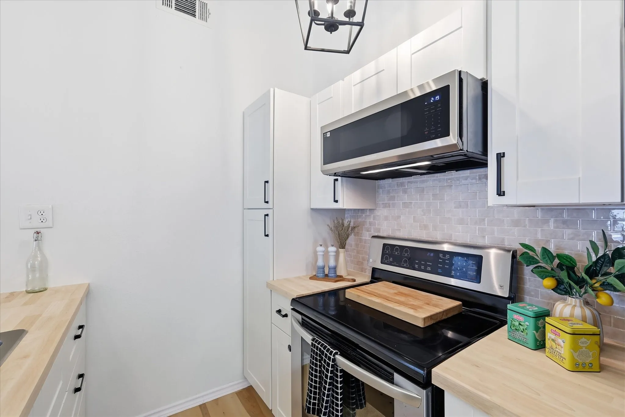 White shaker cabinetry, stainless steel appliances, light wood-finish countertops, and a tiled backsplash