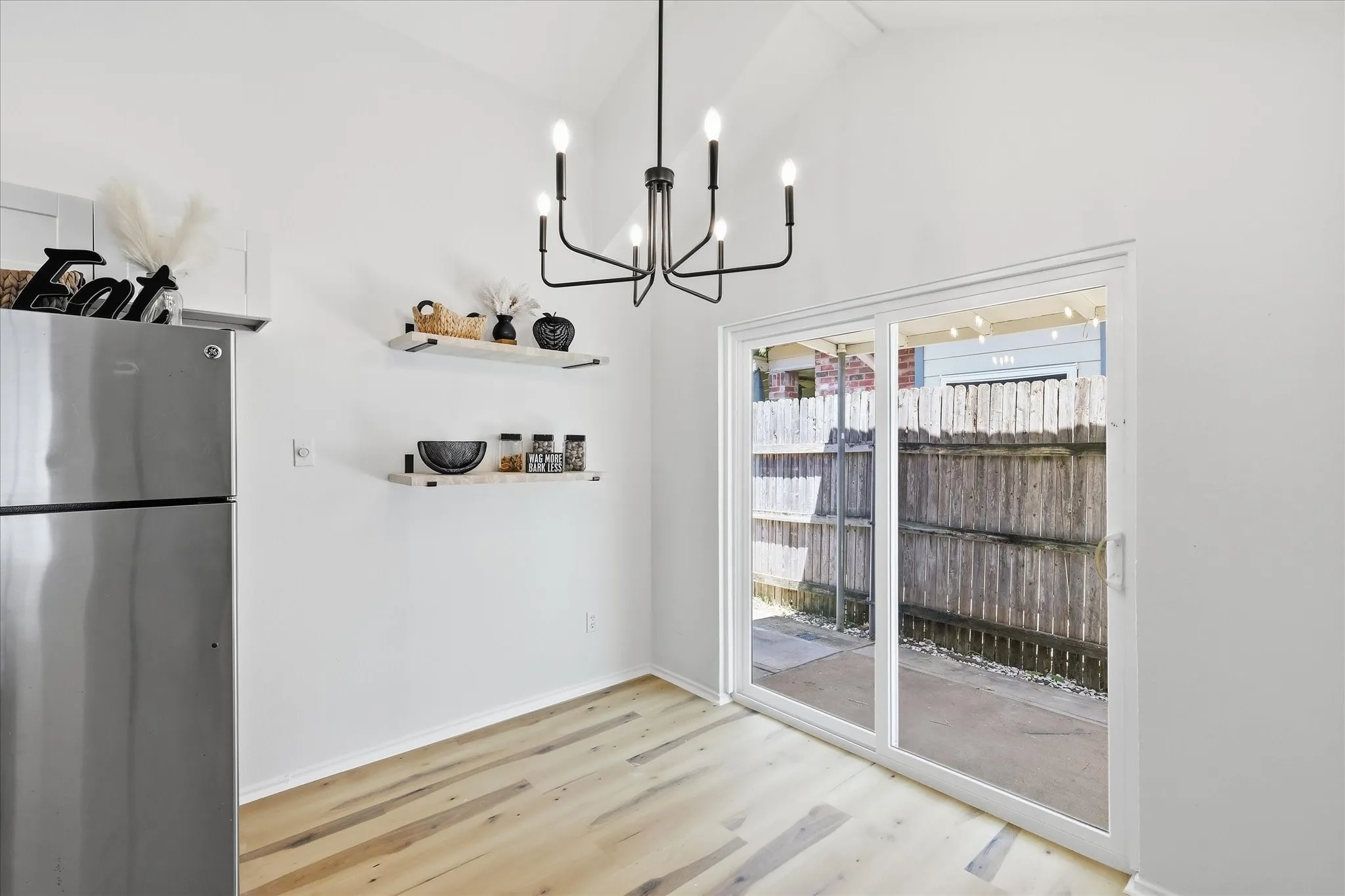 Vaulted ceiling with a black chandelier, light wood-finish flooring, and white walls