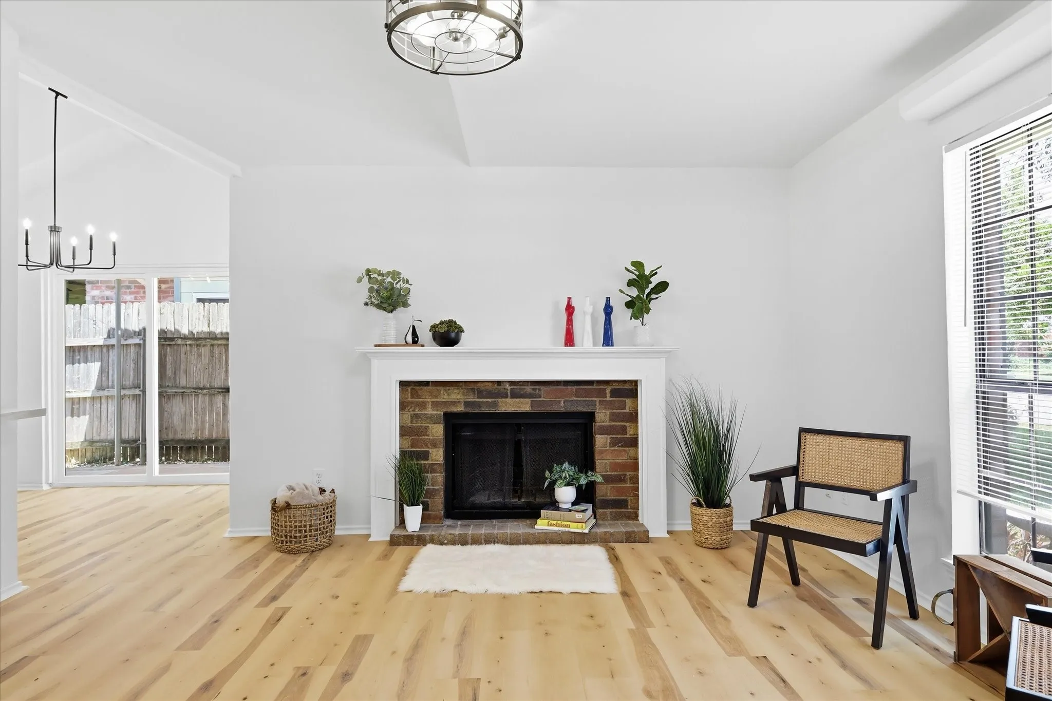 Vaulted ceiling, brick-surround fireplace with a white mantel, wood-finish flooring, sliding glass door, and window with horizontal blinds