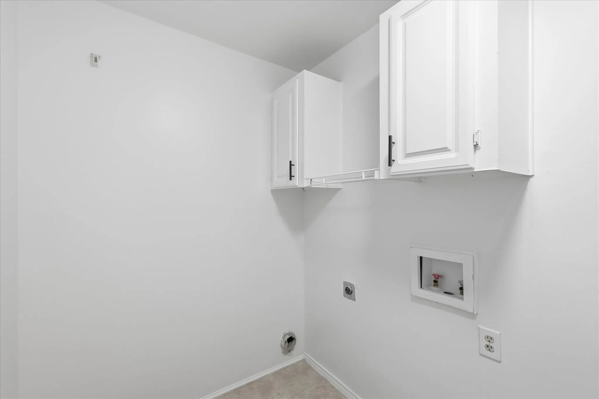 White shaker-style cabinetry with matte black hardware, utility hookups, and light-colored tile flooring