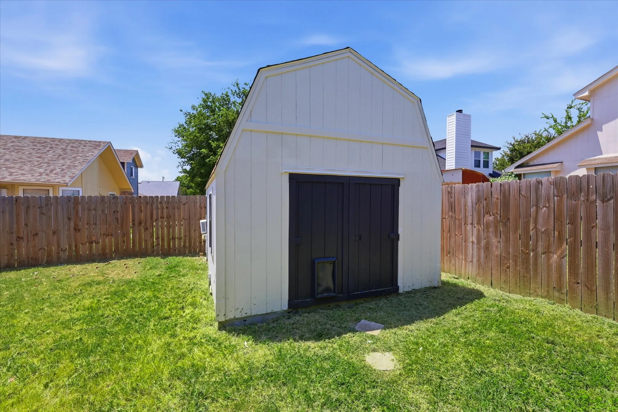 Backyard featuring a shed with white siding, dark double doors, and a gable roof design