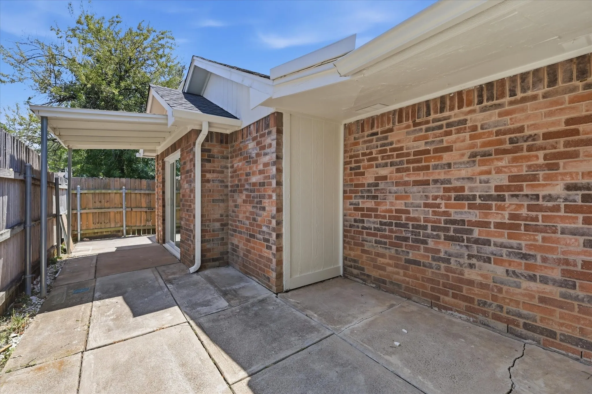 Brick exterior with a covered patio, concrete slab, and wood privacy fencing