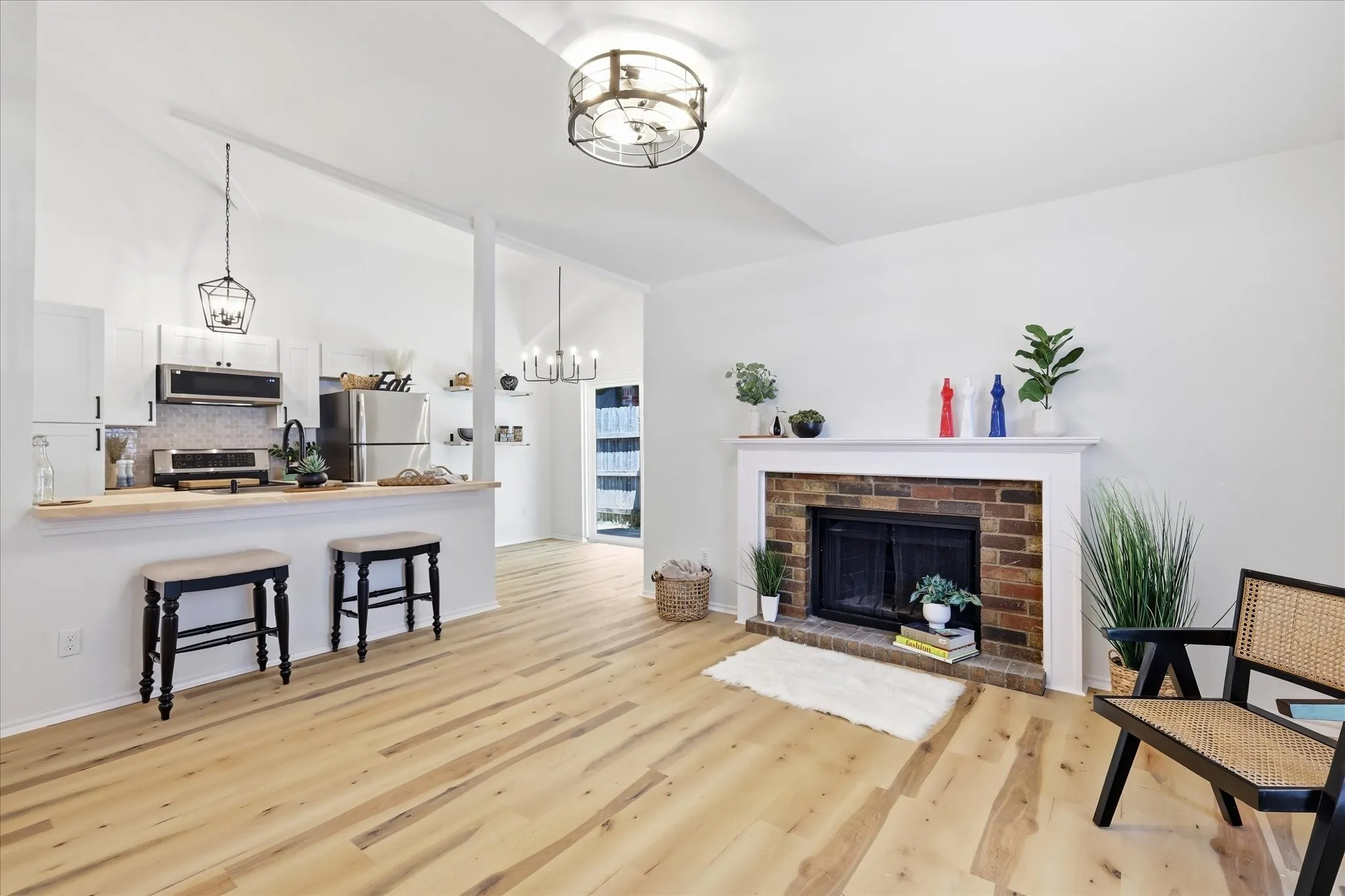 Vaulted ceiling with a contemporary chandelier, light wood-finish flooring, and a brick fireplace with a white mantel