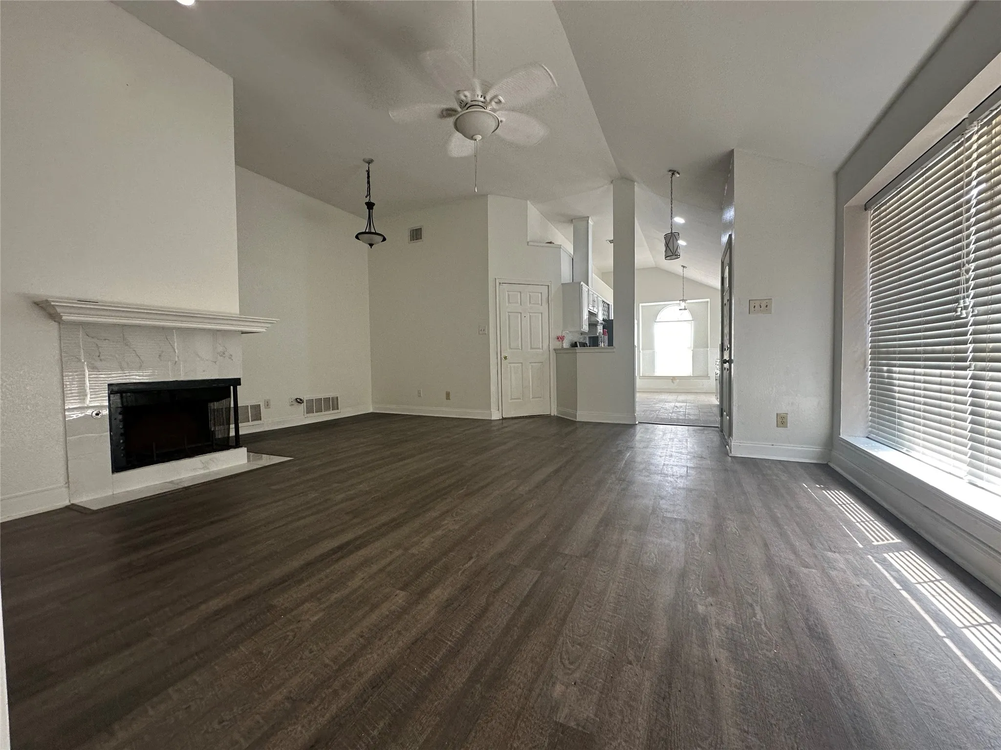 Spacious living area featuring wood-finish flooring, a fireplace with a white tile surround, vaulted ceilings, and a ceiling fan