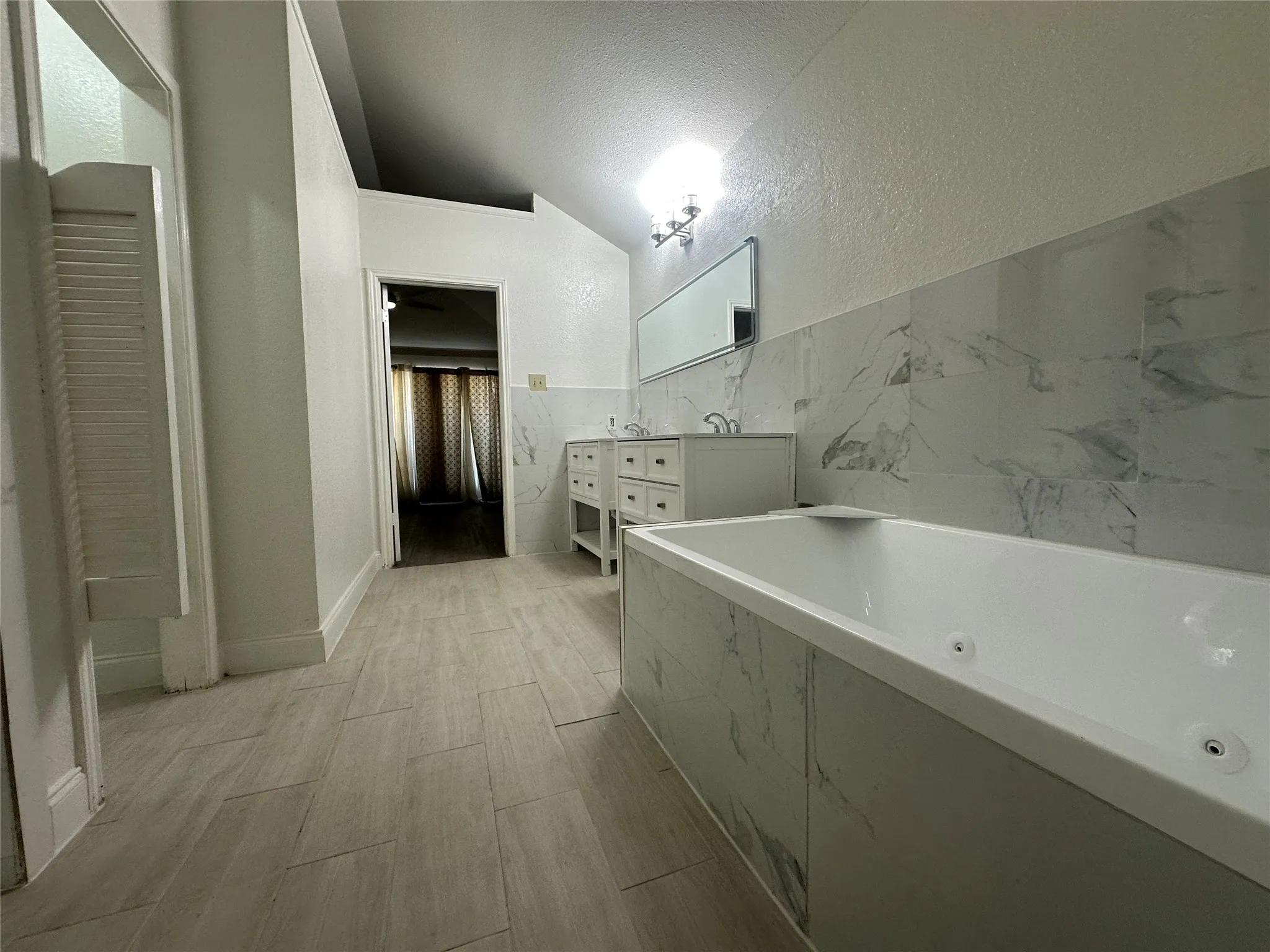 Soaking tub, dual vanity, tile flooring, wall-mounted light fixture, tiled walls
