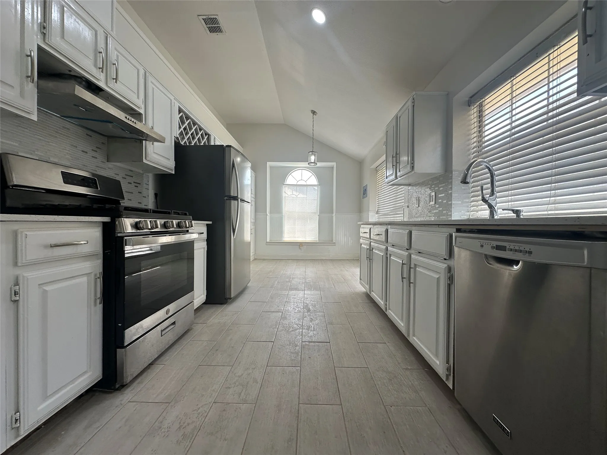 Kitchen featuring white cabinetry, stainless steel appliances, tile flooring, and a vaulted ceiling