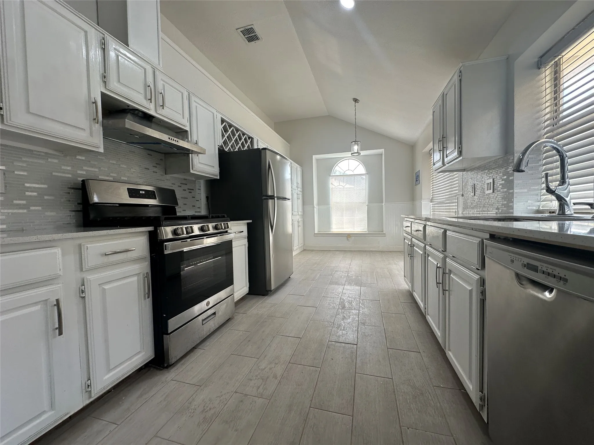 Kitchen featuring white cabinetry, gray tile backsplash, stainless steel appliances, and tile flooring