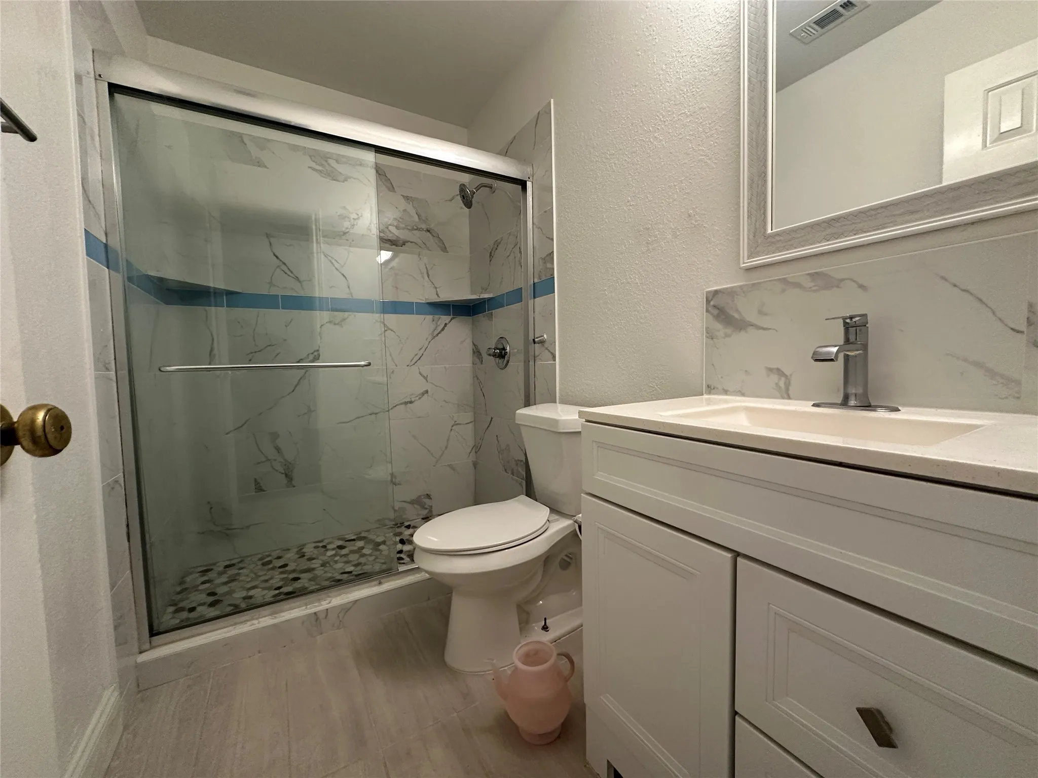 Shower with sliding glass enclosure, white vanity with integrated sink, and framed mirror