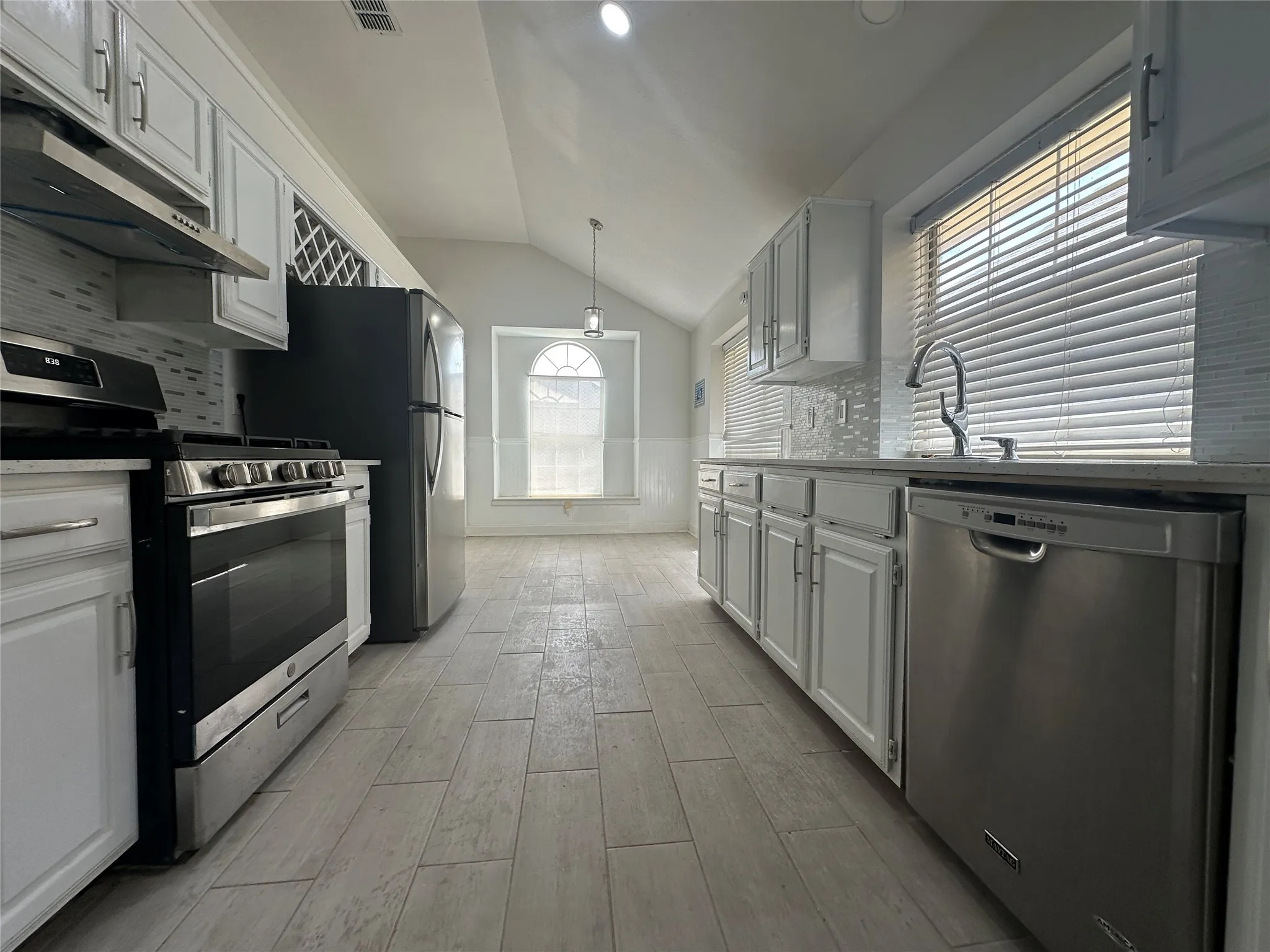 Kitchen featuring stainless steel appliances, tile flooring, white cabinetry, and a tile backsplash