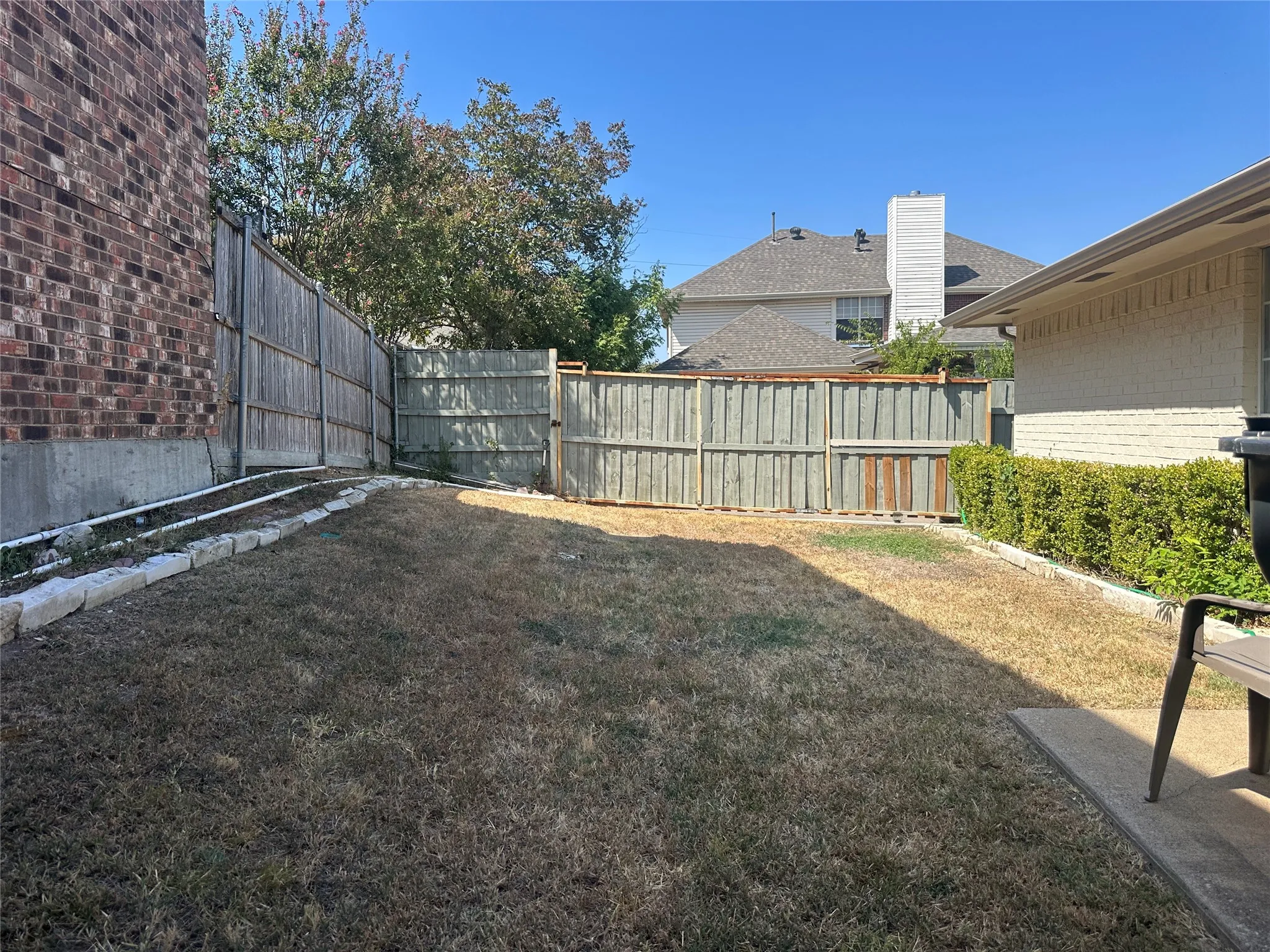 Brick exterior wall, wood privacy fencing, stone border landscaping, paved patio area, green hedging
