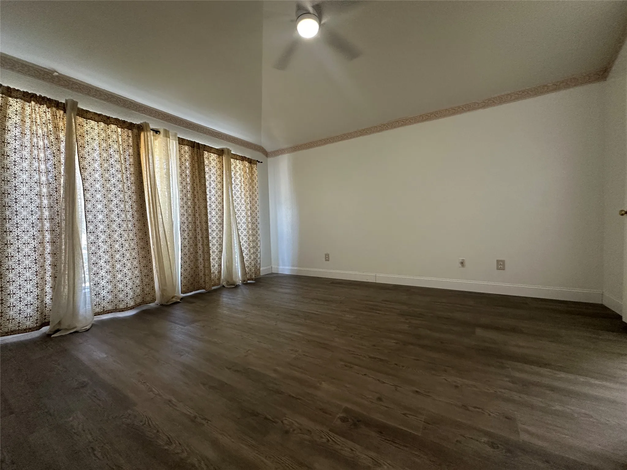 Vaulted ceiling, wood-finish flooring, ceiling fan, and white walls