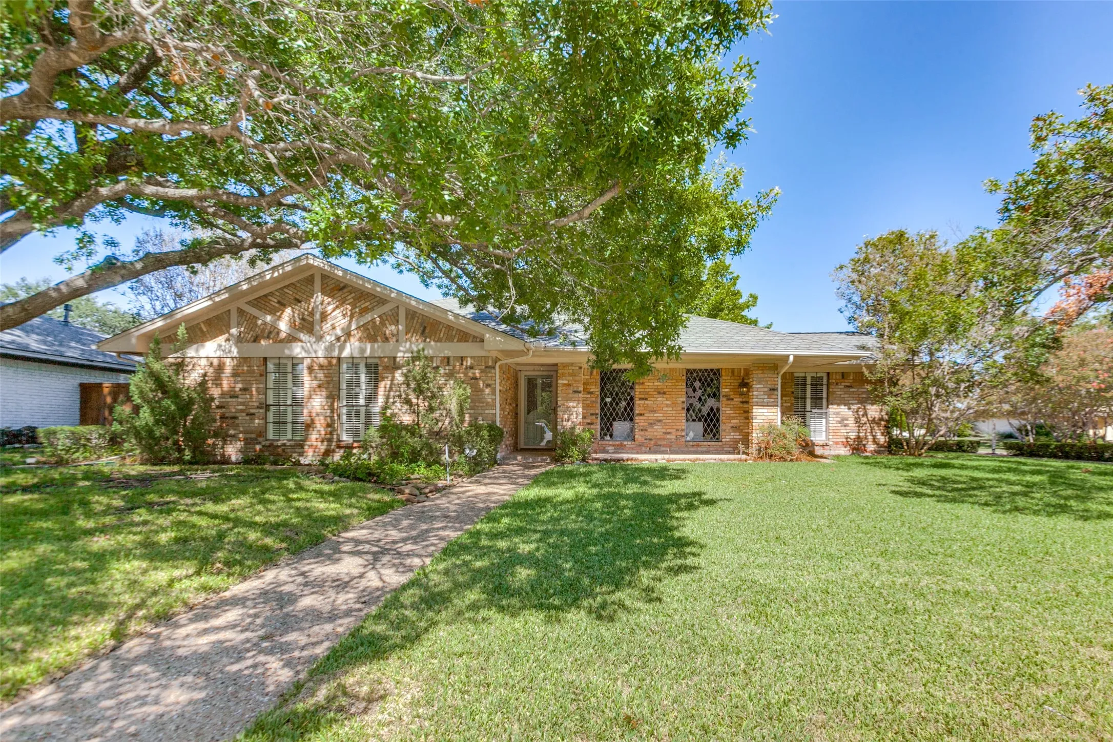 915 Grinnell Dr. - Front exterior of the home situated on a large corner lot, featuring mature trees, established landscaping, and a spacious covered front porch.