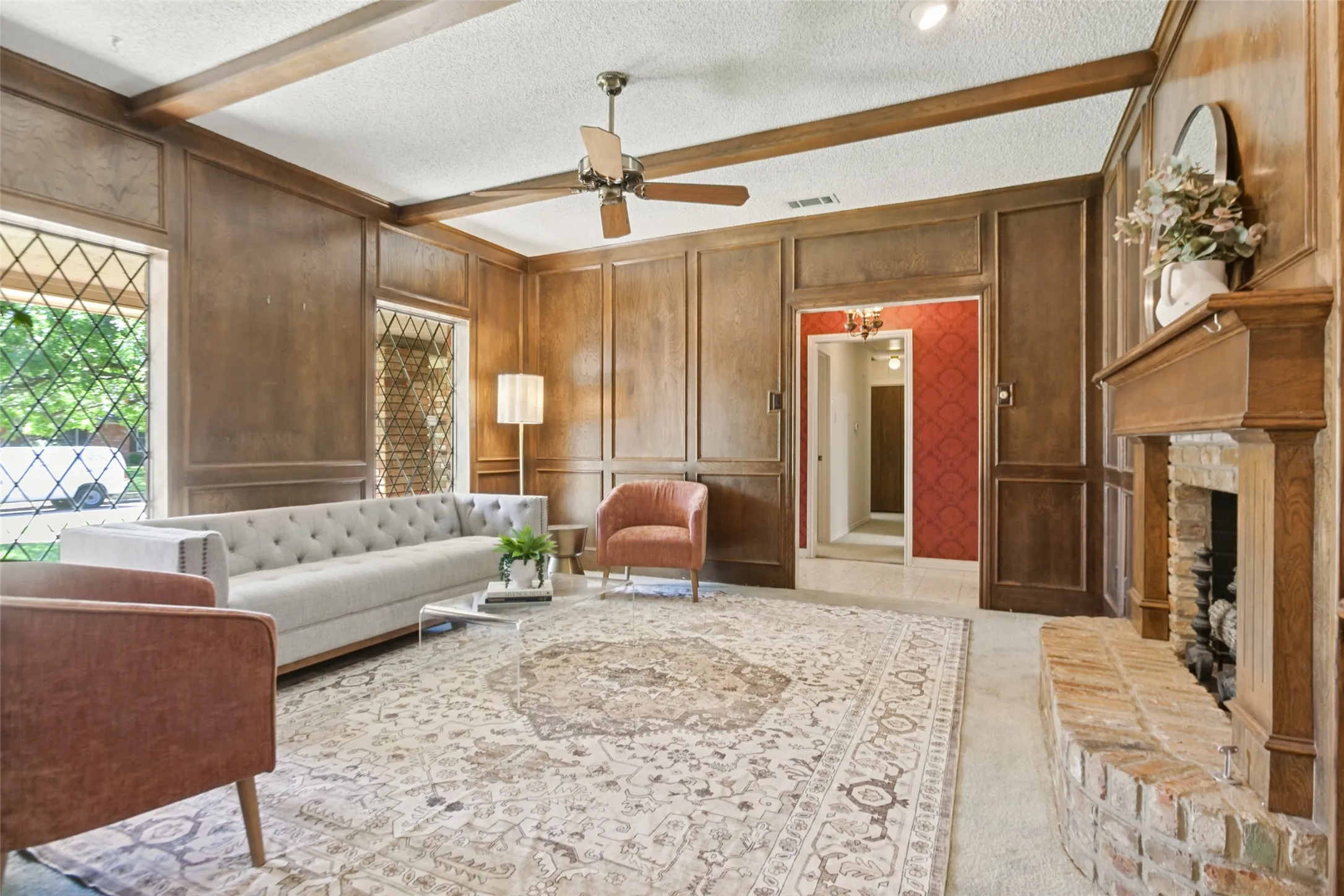 915 Grinell Dr. - Formal living area featuring wood picture-frame paneling, wood beams, ceiling fan, brick fireplace with gas-log insert, and beautiful windows providing abundant natural light.