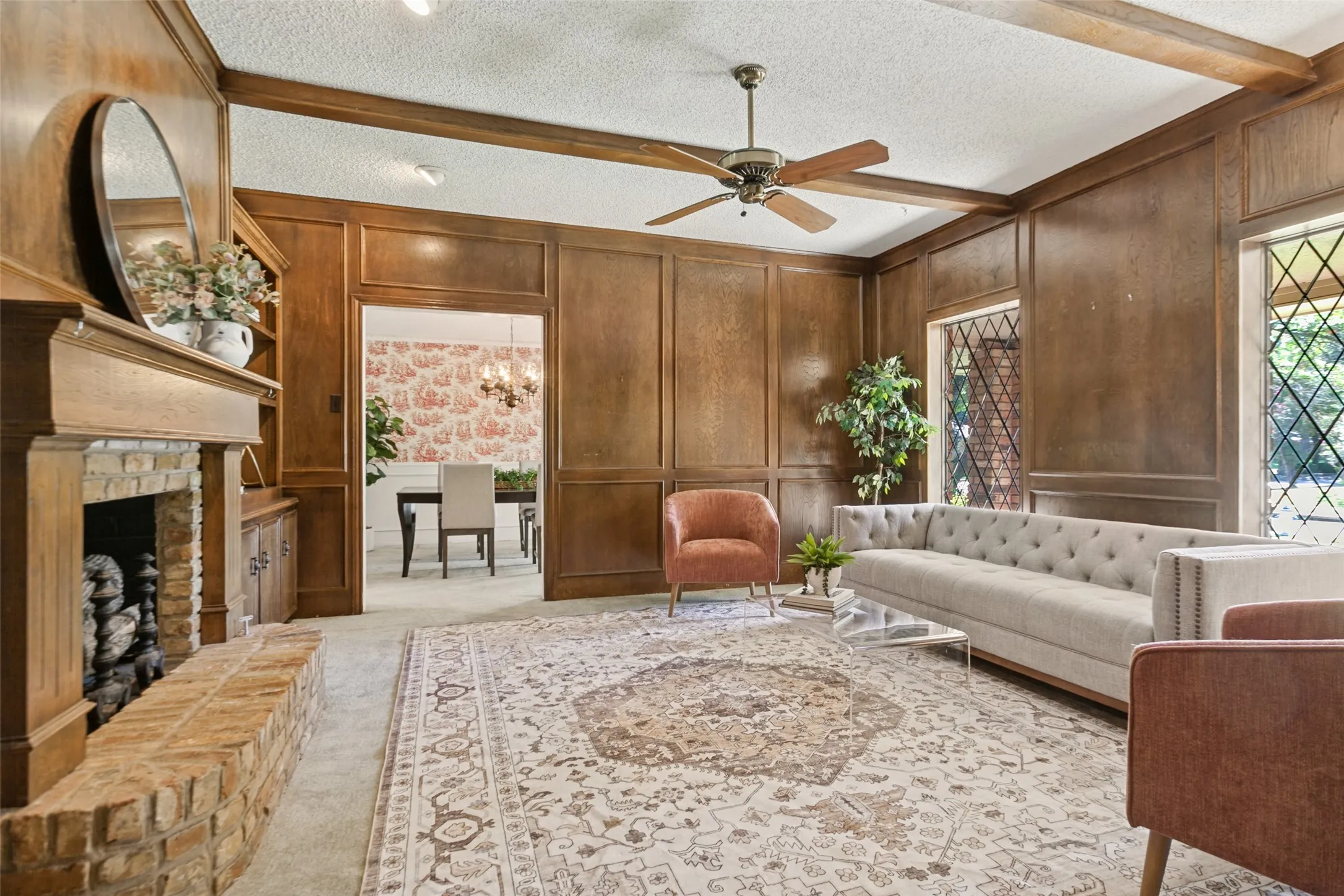 915 Grinell Dr. - Formal living area featuring wood picture-frame paneling, wood beams, ceiling fan, brick fireplace with gas-log insert, and beautiful windows providing abundant natural light.