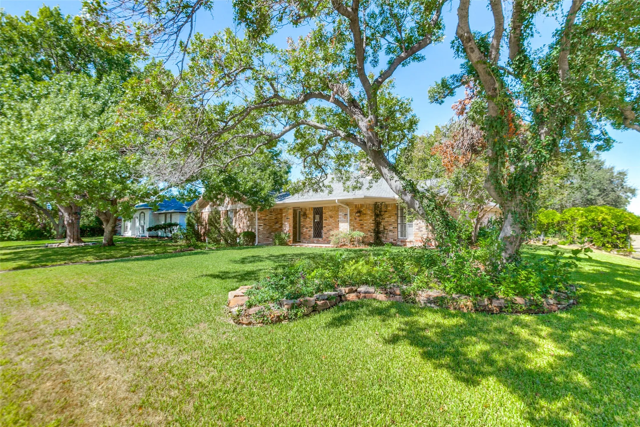 915 Grinnell Dr. - Front exterior of the home situated on a large corner lot, featuring mature trees, established landscaping, and a spacious covered front porch.