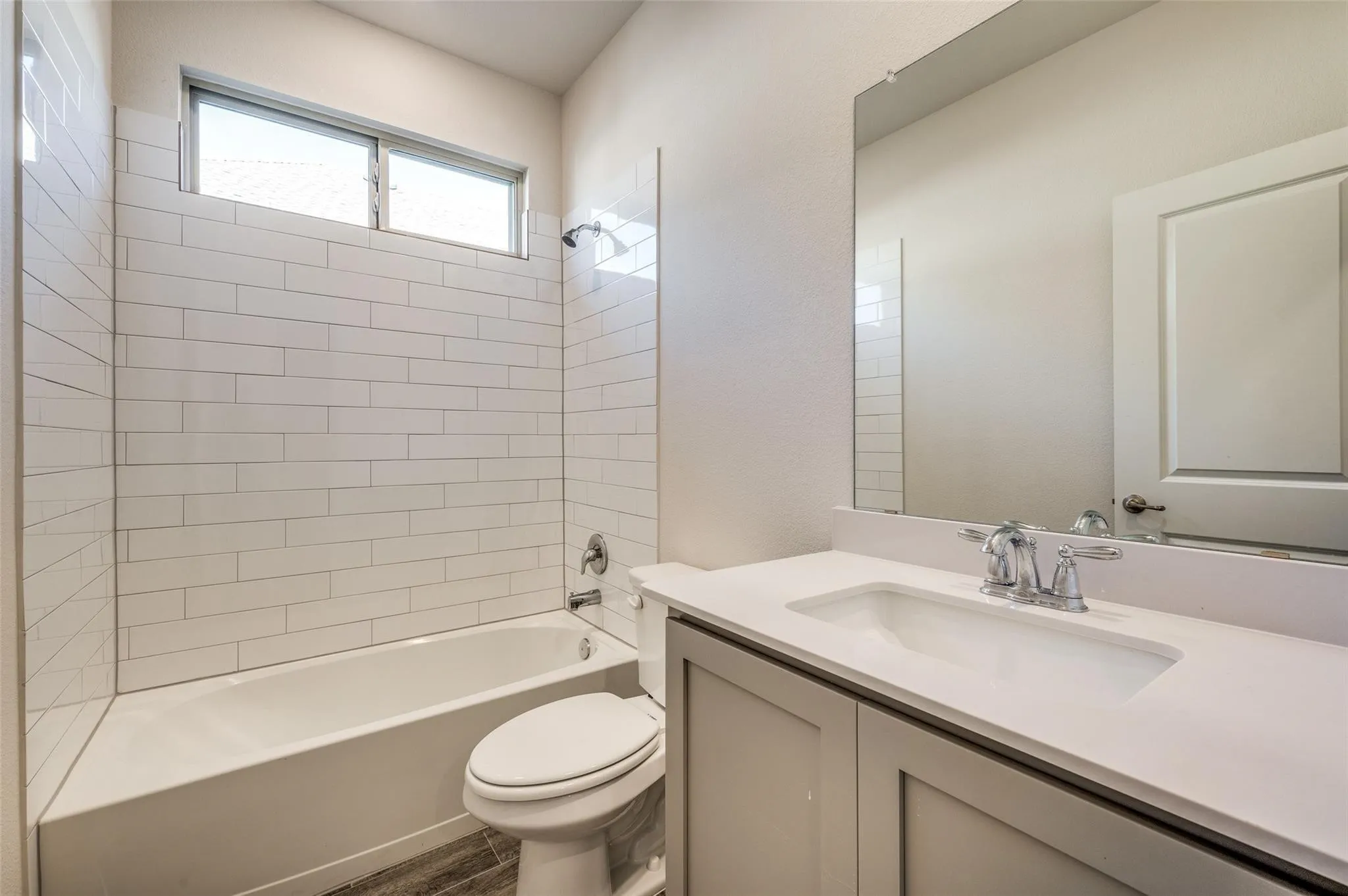 White subway tile bath surround, chrome fixtures, built-in tub, vanity with integrated sink, and wood-finish flooring