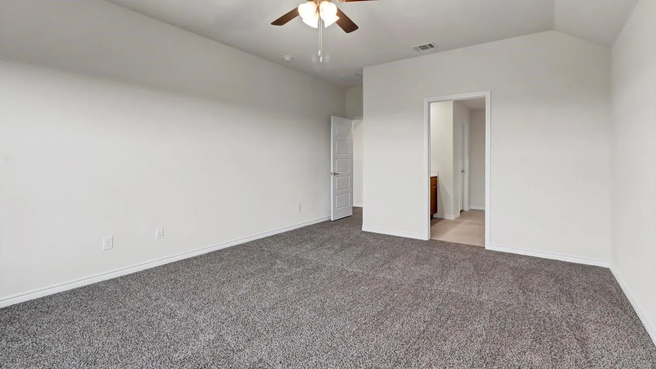 Spacious room featuring vaulted ceilings, gray carpet, and a ceiling fan with integrated lighting