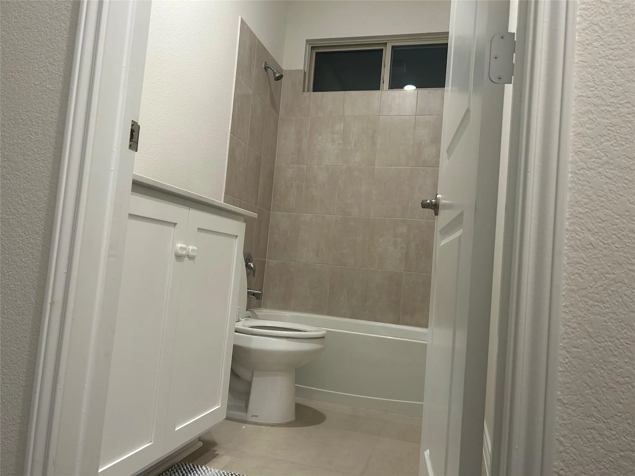 White vanity with cabinet storage, tiled shower surround, integrated bathtub, and a window for natural light