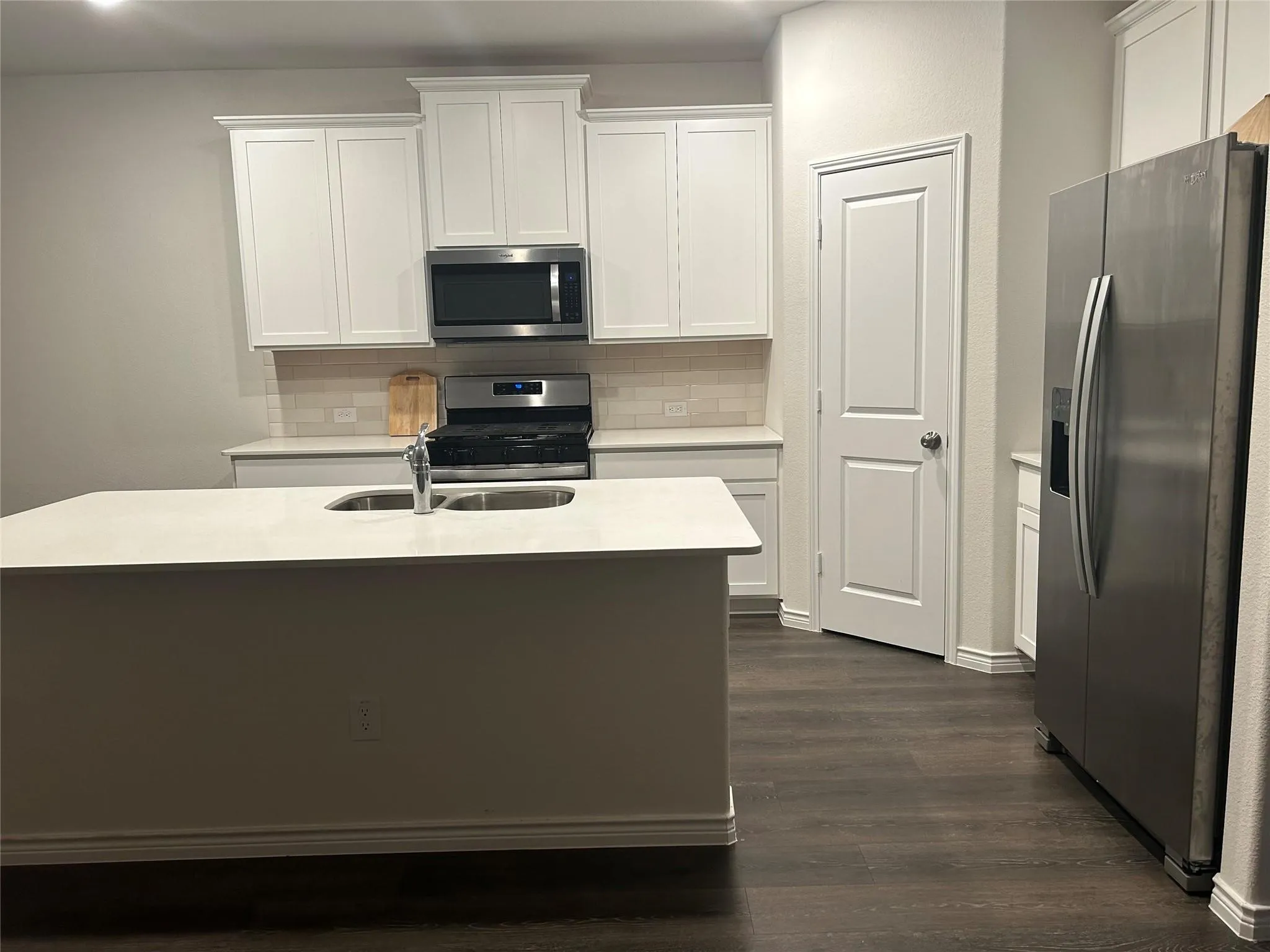 Kitchen featuring an island with an undermount sink, white cabinetry, stainless steel appliances, and wood-finish flooring