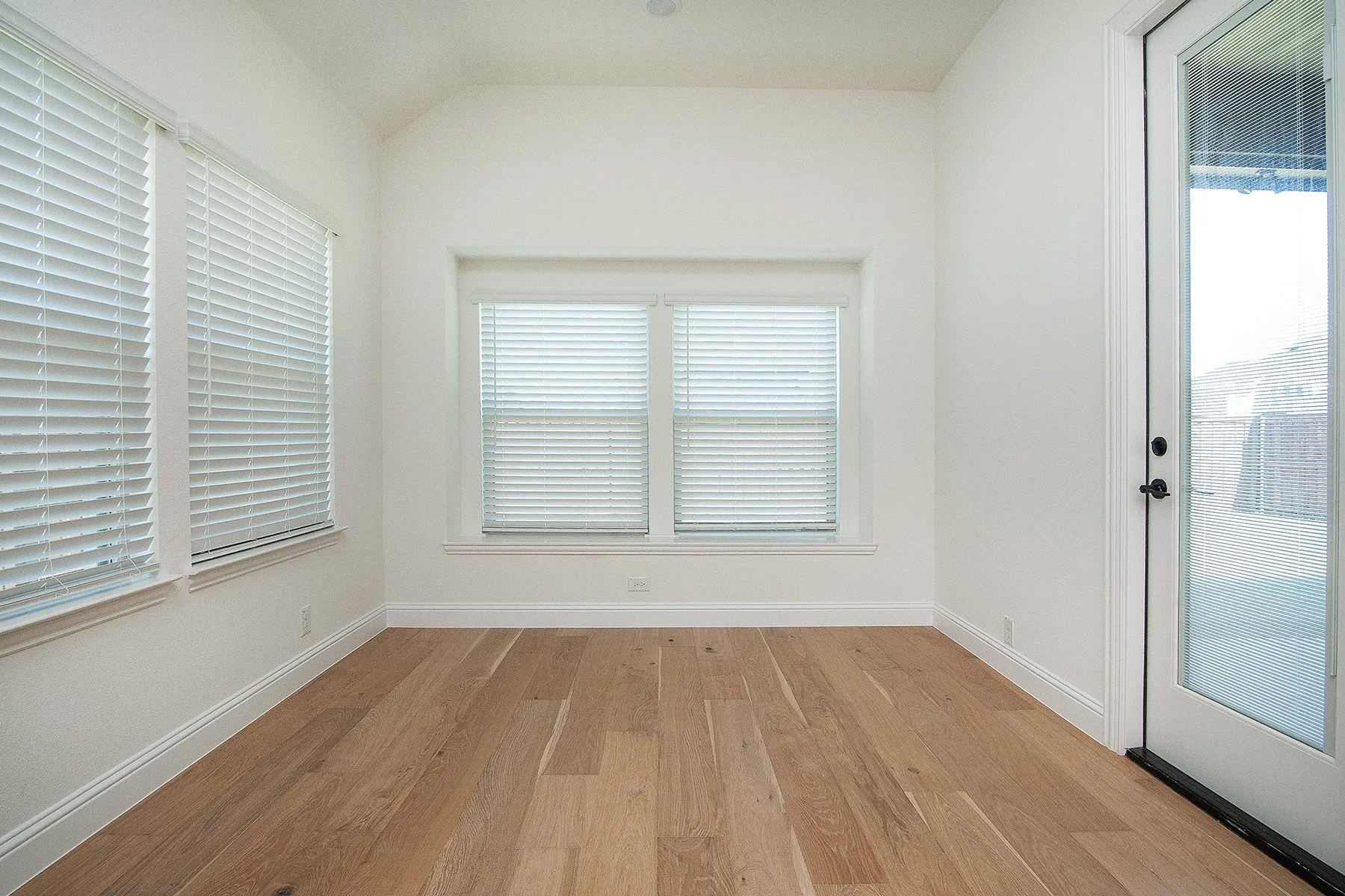 Wood-finish flooring, multiple windows with blinds, pitched ceiling, and a glass-paneled exterior door