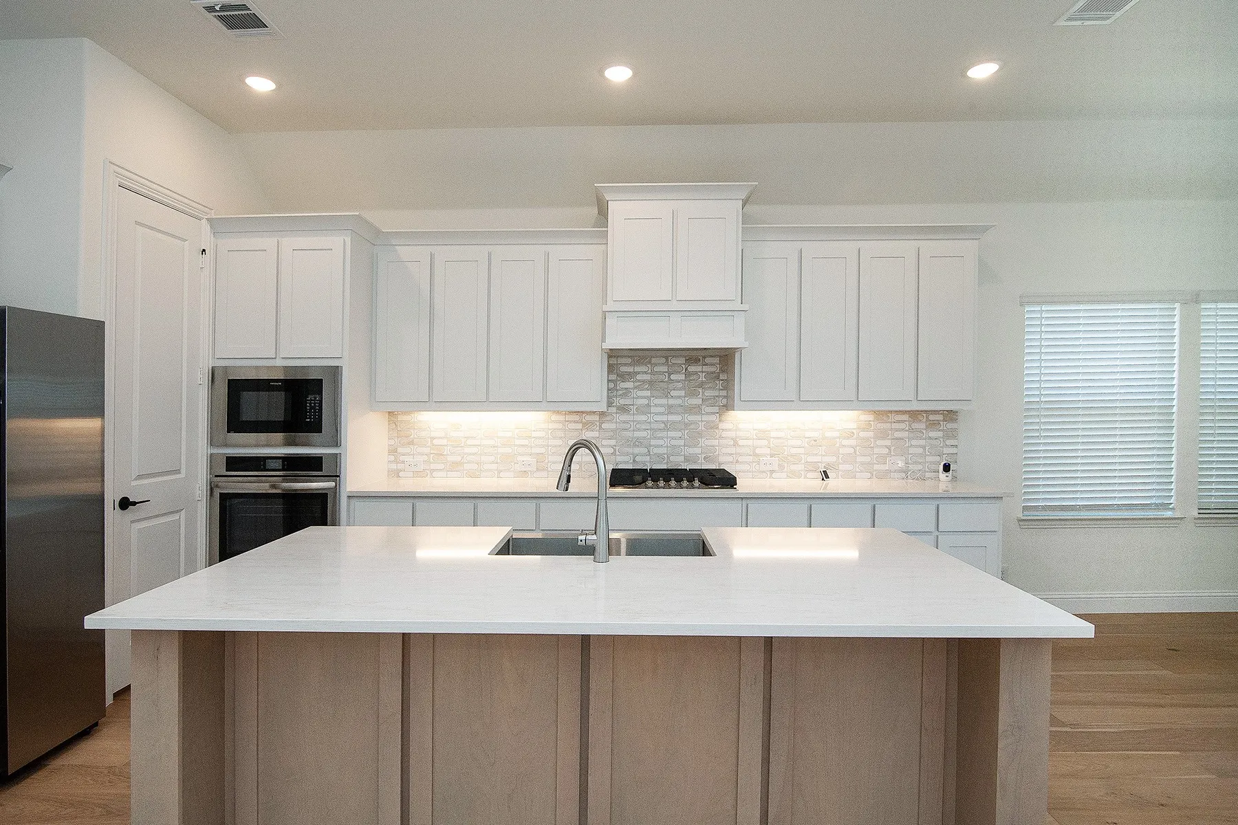 Central kitchen island with white countertop, white shaker-style cabinetry, stainless steel appliances, tile backsplash, and recessed lighting