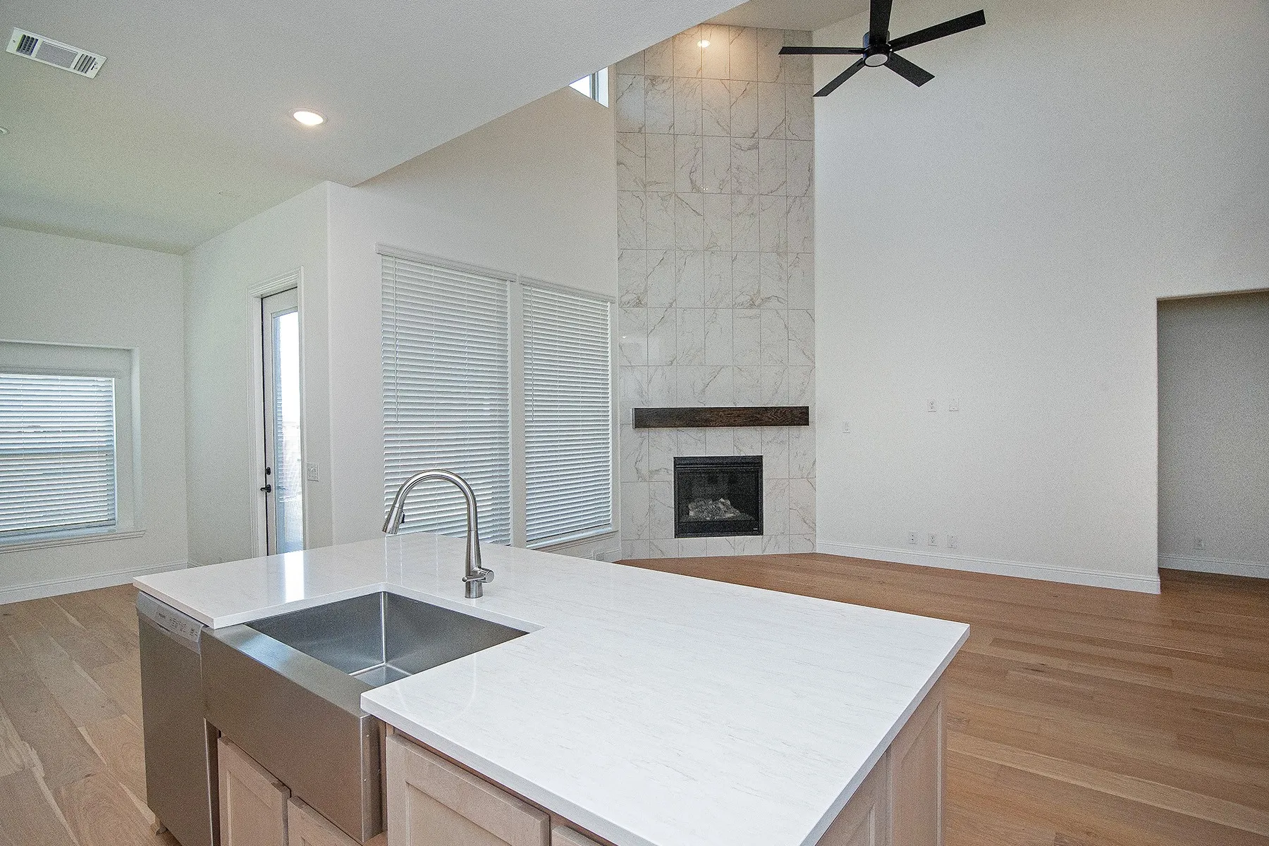Vaulted ceilings enhance the open concept living space, featuring a fireplace with a stone-finish facade, a wood mantle, and a ceiling fan