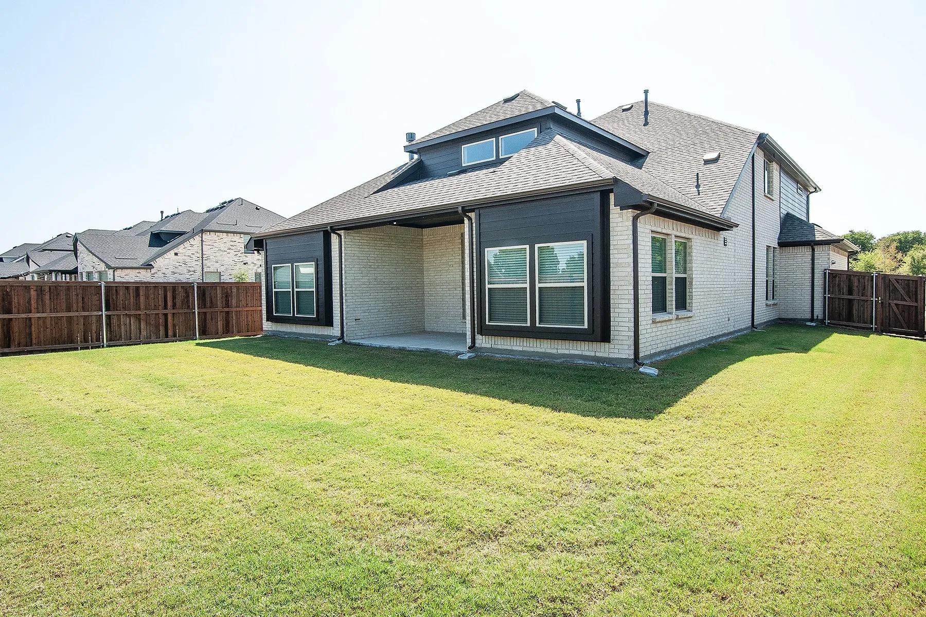 Spacious backyard featuring a covered patio, wood privacy fencing, and a light brick exterior